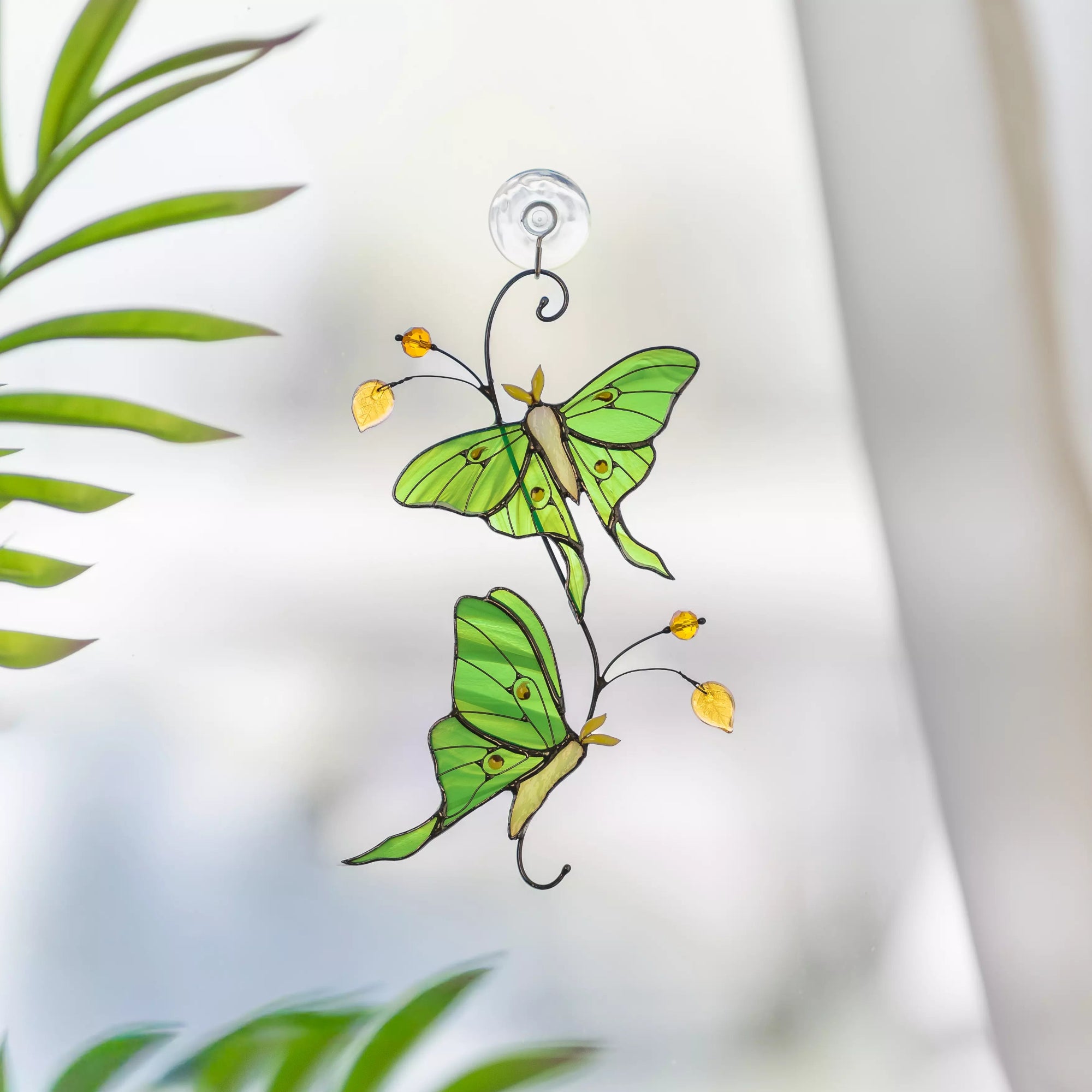 Stained glass suncatcher featuring two green luna moth butterflies with leaves in the background