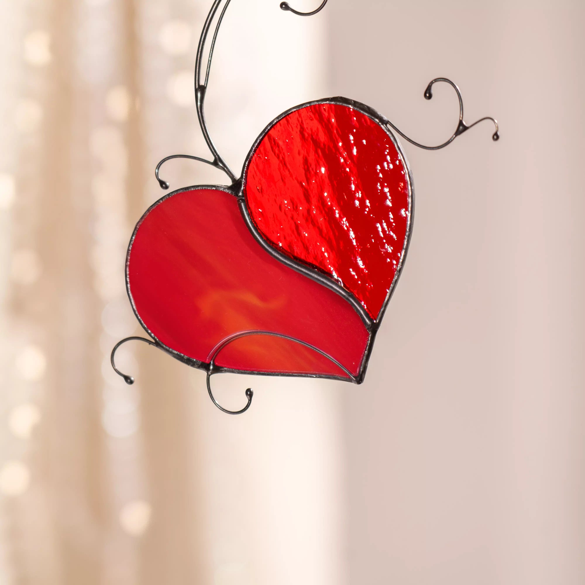 Close up view of stained glass heart-shaped window hanging with a red design on a beige background