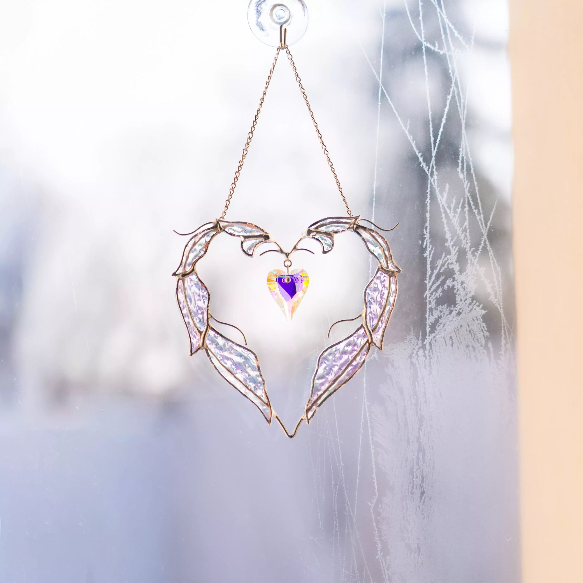 Handmade stained glass heart suncatcher displayed on a window using a suction cup.