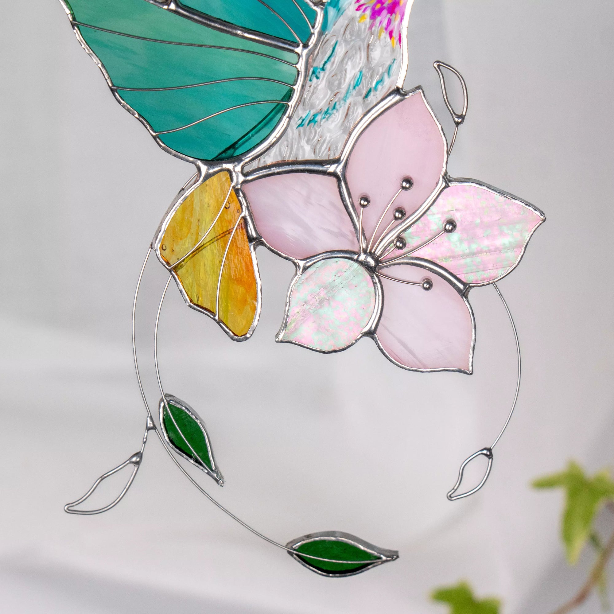 Close-up view of stained glass hummingbird and flower suncatcher on a white background