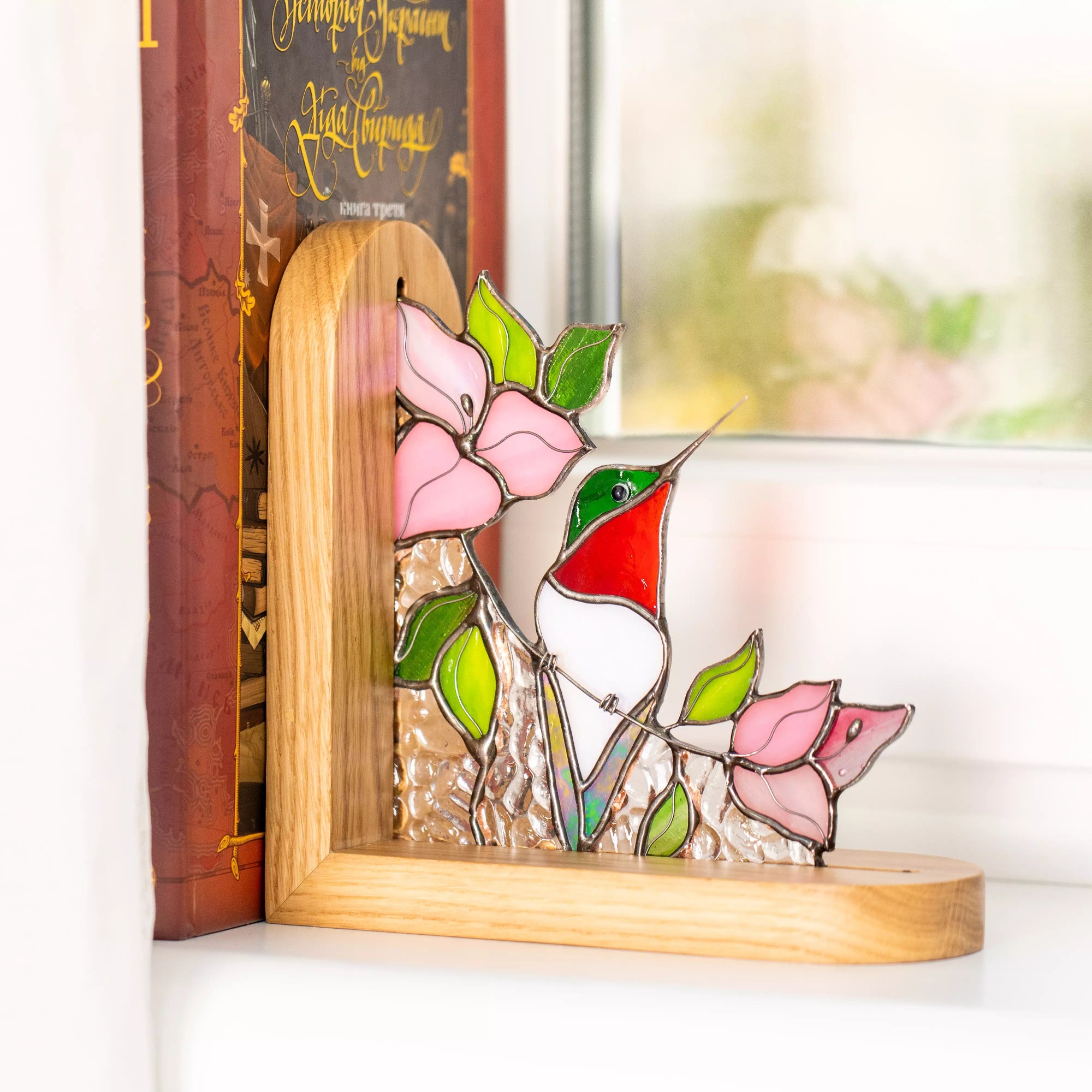 Stained glass hummingbird bookend standing near a window, surrounded by floral glass details.