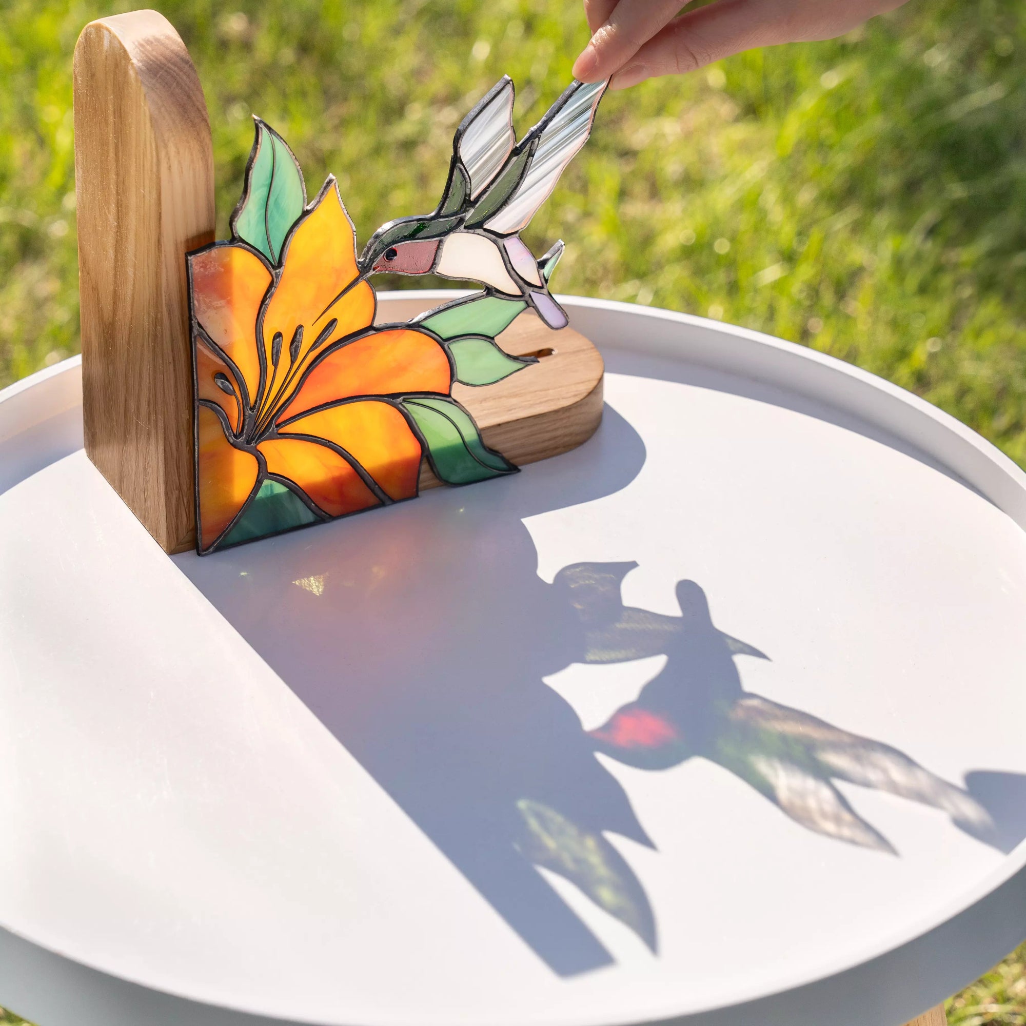 Hand adjusting stained glass hummingbird bookend outdoors with sunlight casting colorful shadows