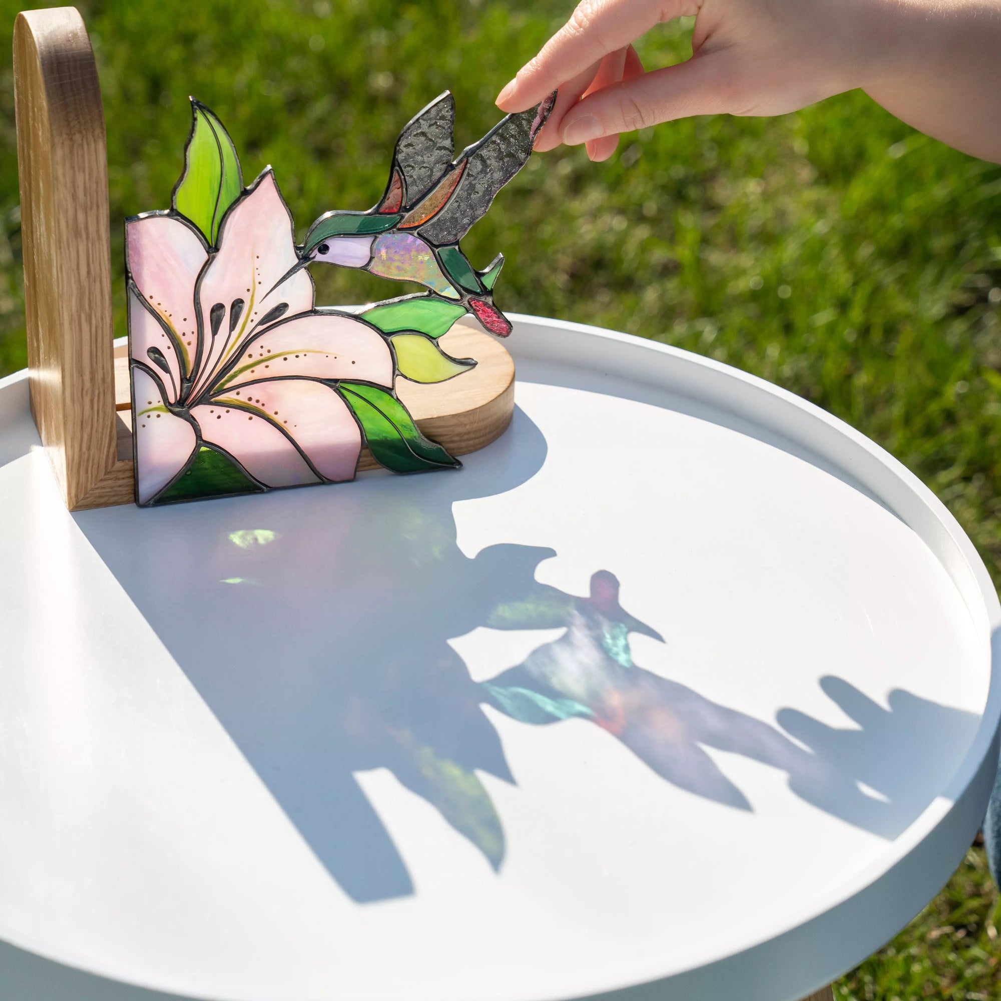 Hand adjusting stained glass hummingbird bookend outdoors with sunlight and soft shadows