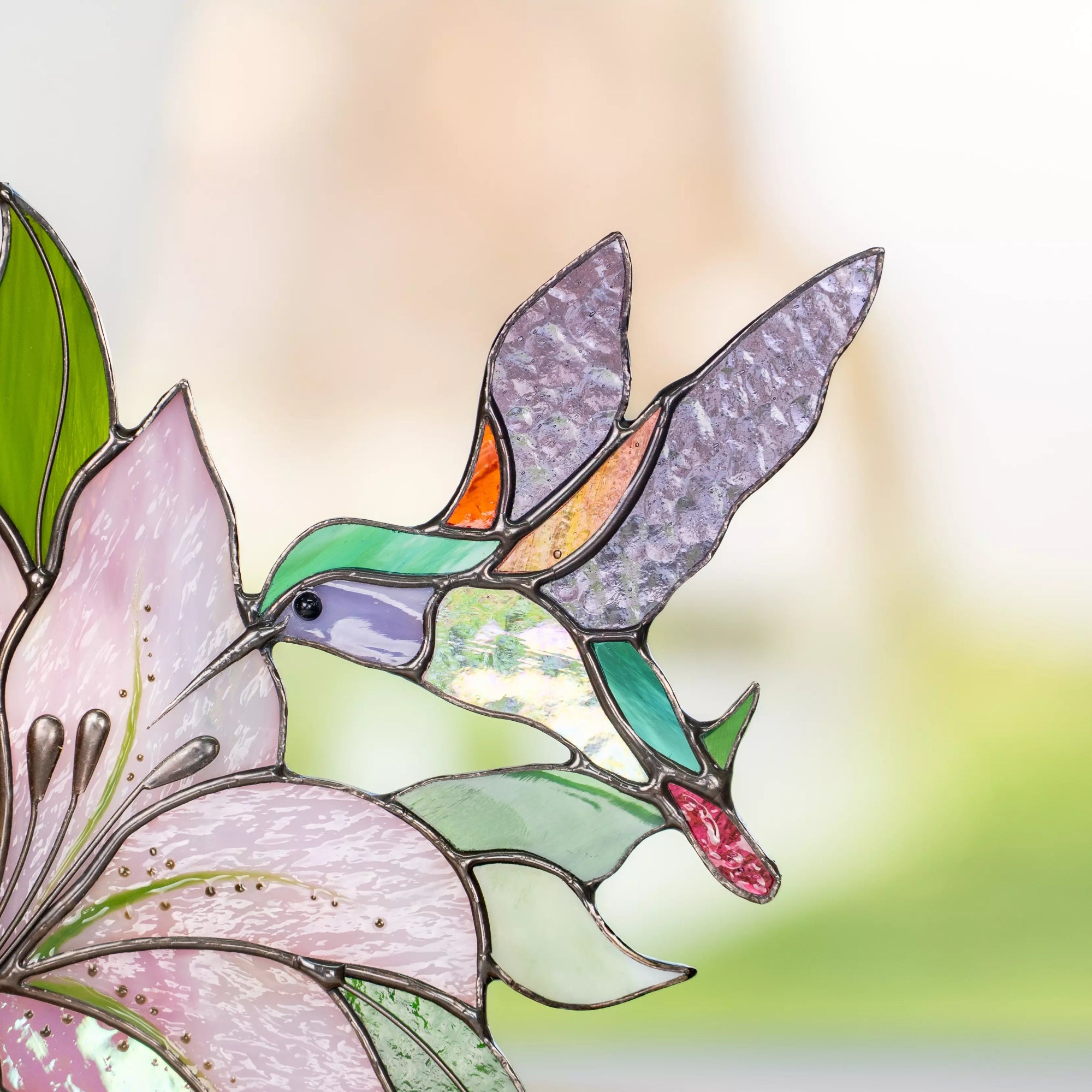 Close-up of stained glass hummingbird with iridescent wings and pink flower petals