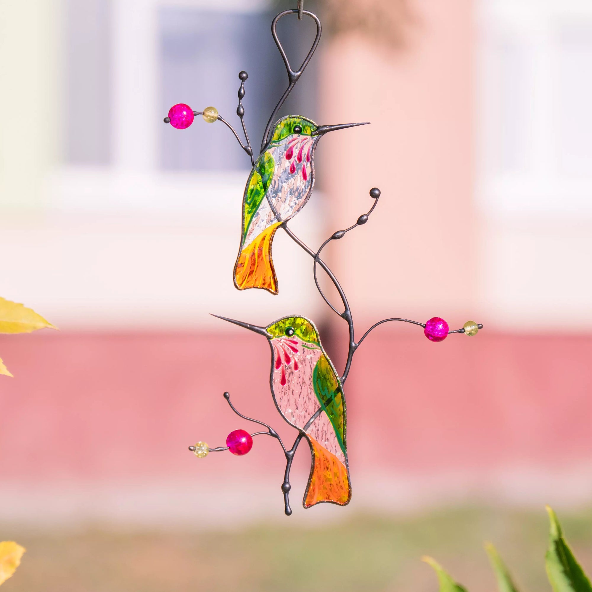 Stained glass hummingbirds suncatcher with pink beads on a blurred natural background