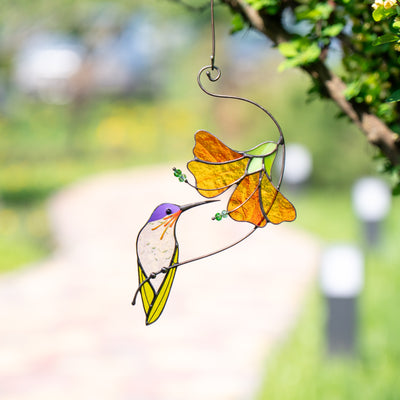 Hanging stained glass hummingbird sipping from orange flower outdoors