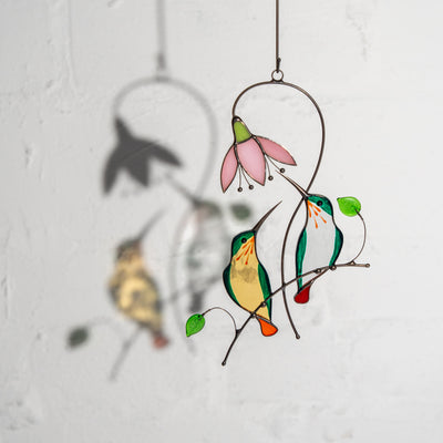 Hanging stained glass green hummingbirds casting a shadow on a white wall.