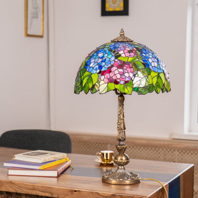 Colorful stained glass lamp with hydrangea flower design and ornate bronze base on wooden desk with books