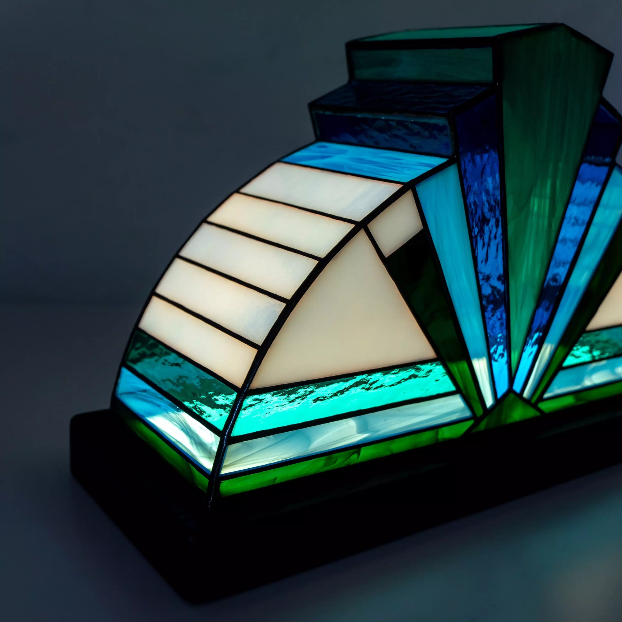 Close-up of handmade blue stained glass lamp glowing warmly, featuring teal and aqua glass textures on a natural wood base.