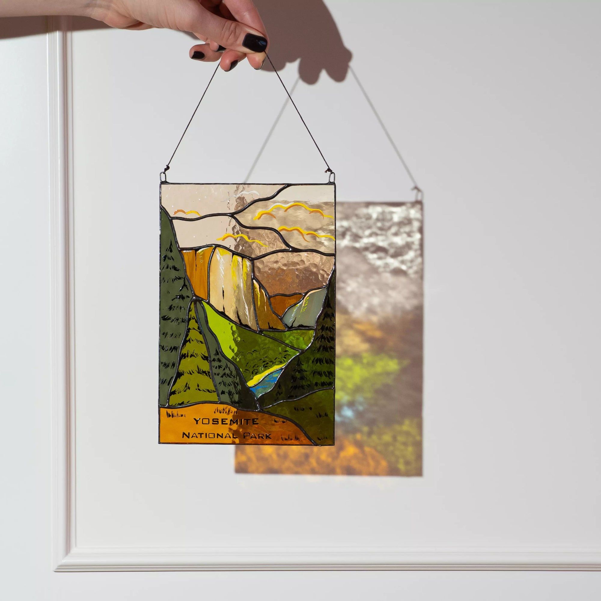 A Yosemite stained glass panel casting a beautiful detailed landscape shadow on a white wall in the sun.