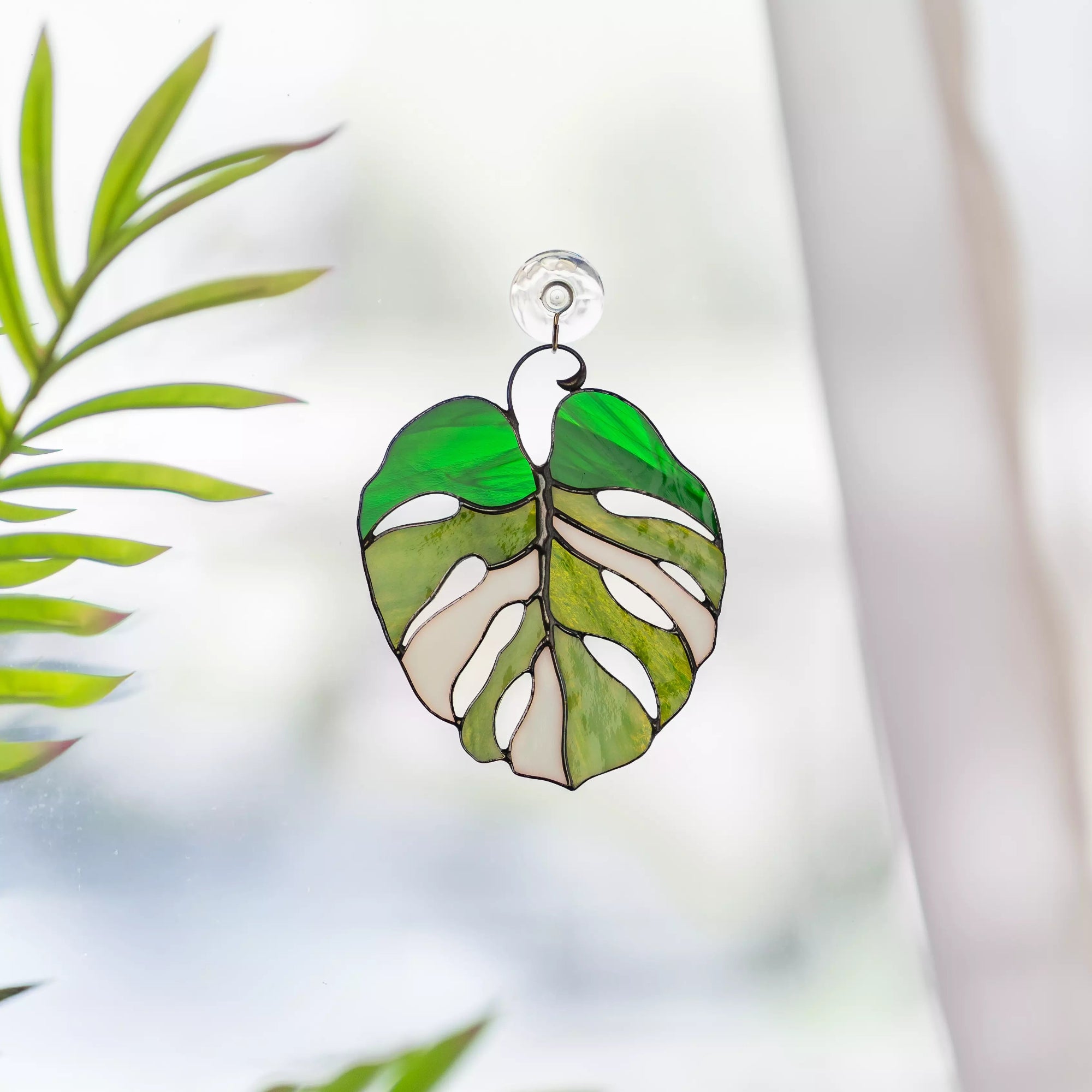 Stained glass monstera leaf suncatcher with green and white design on a blurred natural background