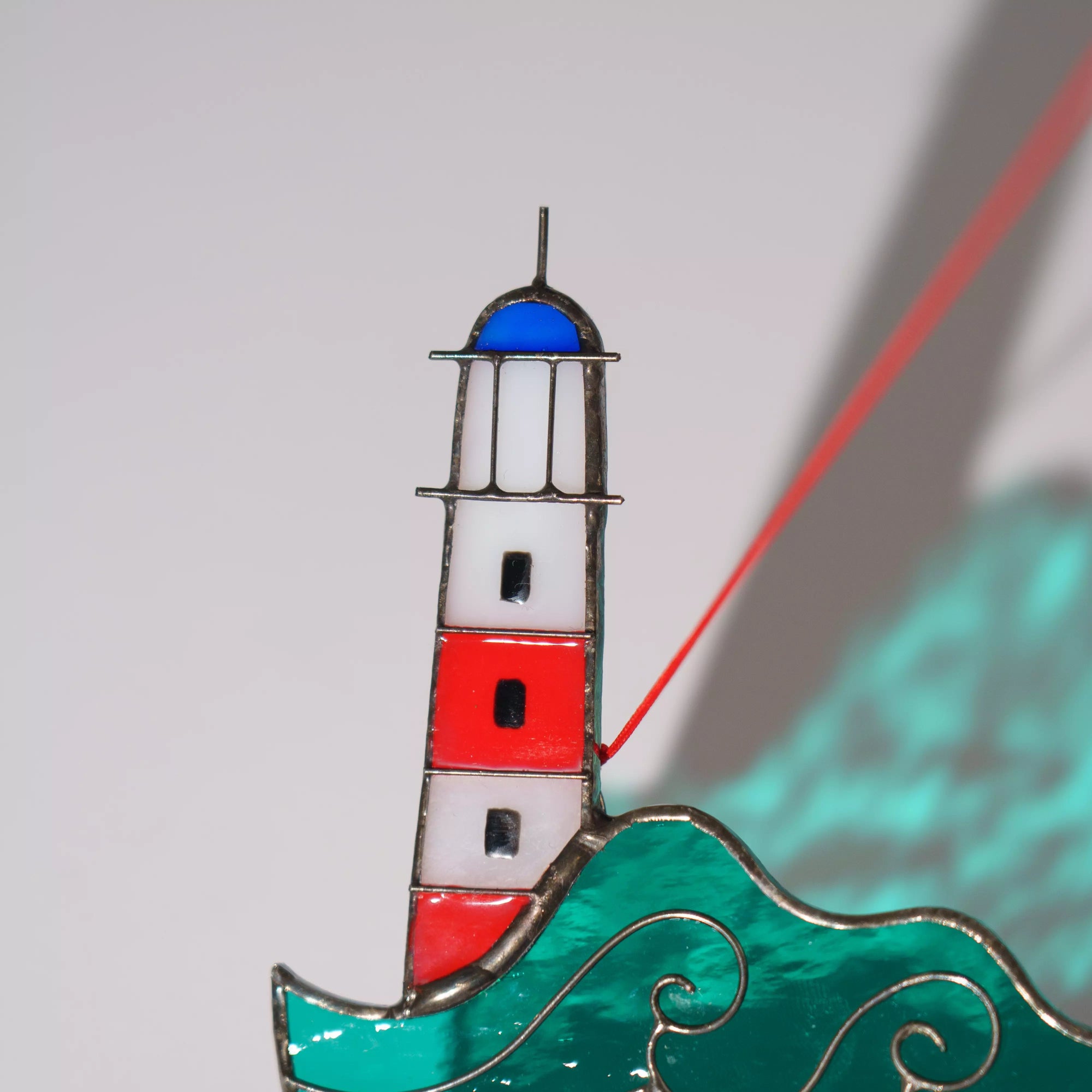Close-up view of stained glass lighthouse decoration on a plain background