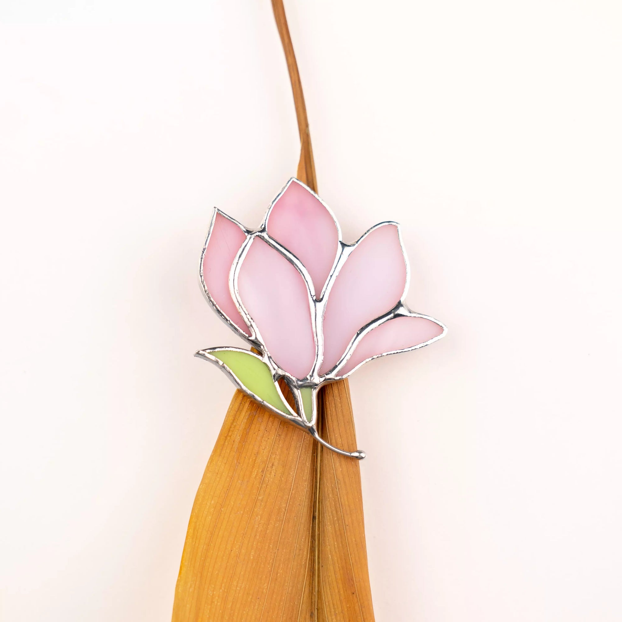 Pink stained glass magnolia brooch with a leaf on background