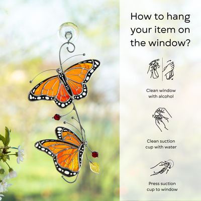 Two orange monarch butterflies hanging on a window, captured in bright natural light with instruction beside: clean window and suction cup, press a cup to the surface.