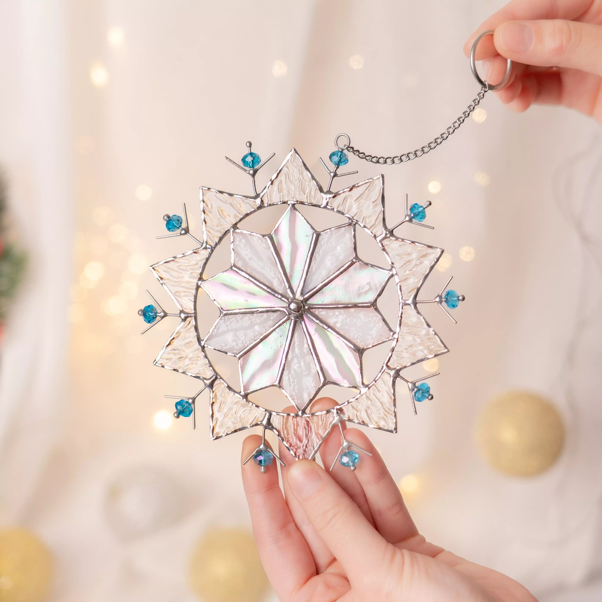 Stained glass snowflake with blue beads held by a hand against a soft, blurred background.