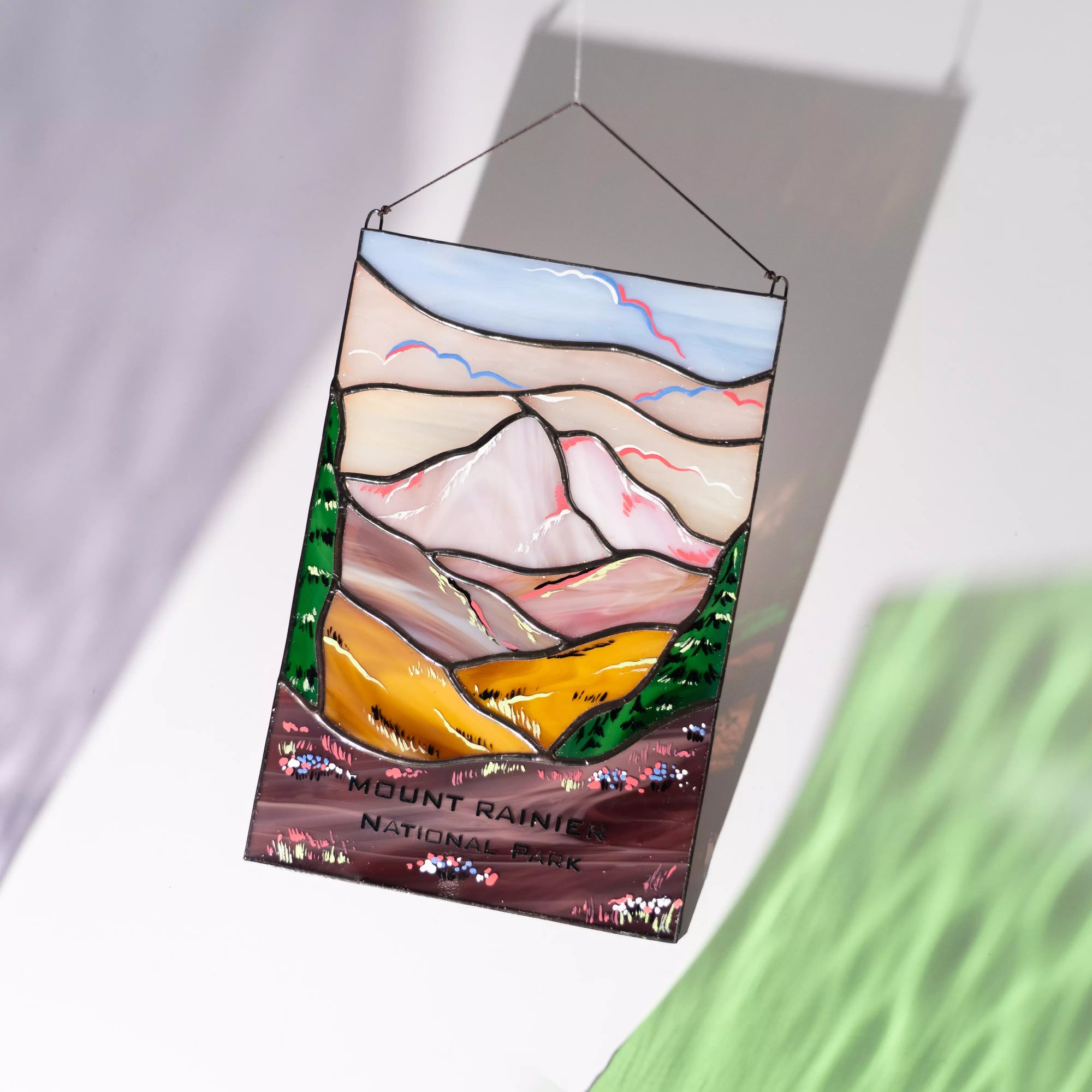A Mount Rainier stained glass panel casting a vibrant purple and white shadow on a wall in the sun.