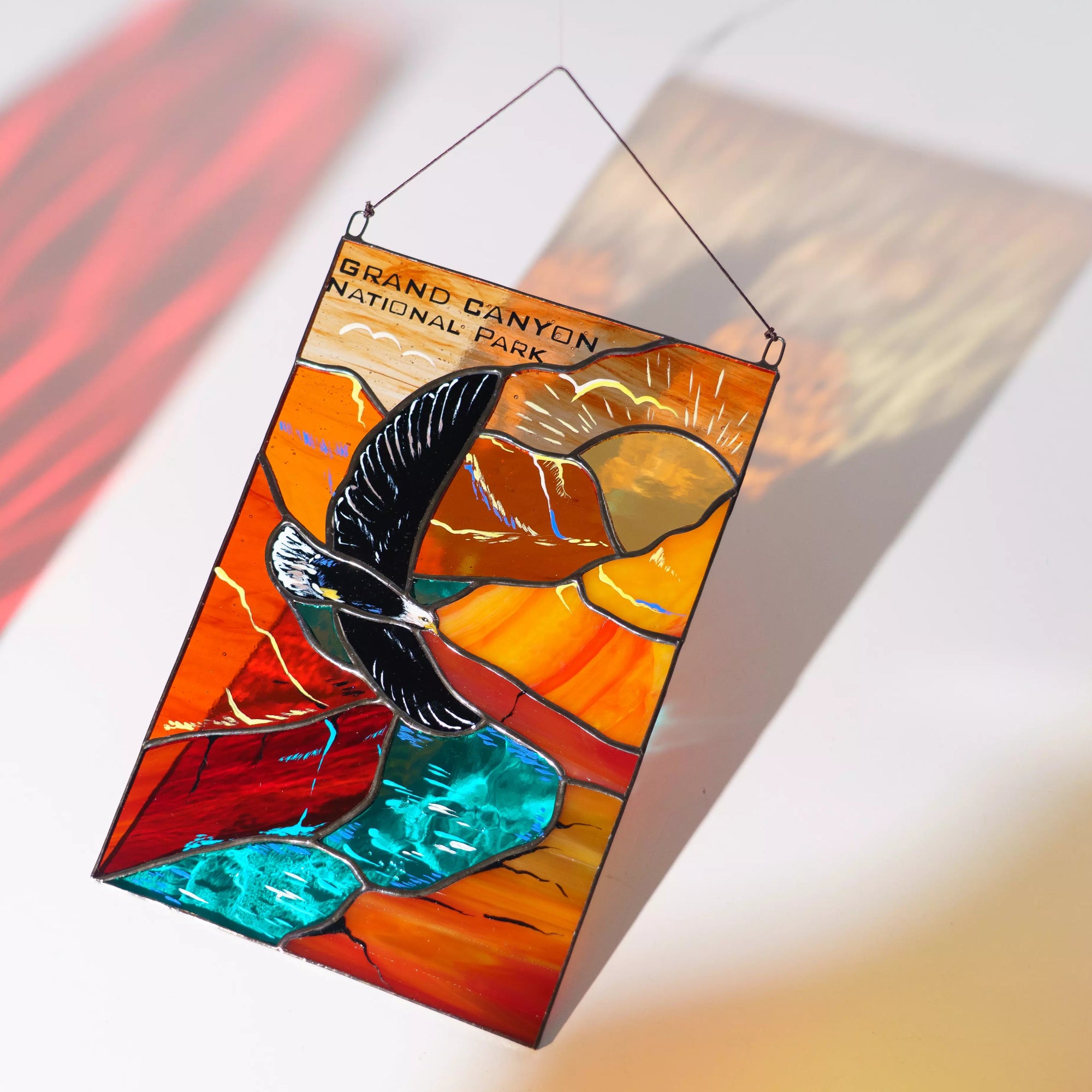 A person holding the Grand Canyon stained glass panel that casts a warm red and turquoise shadow.