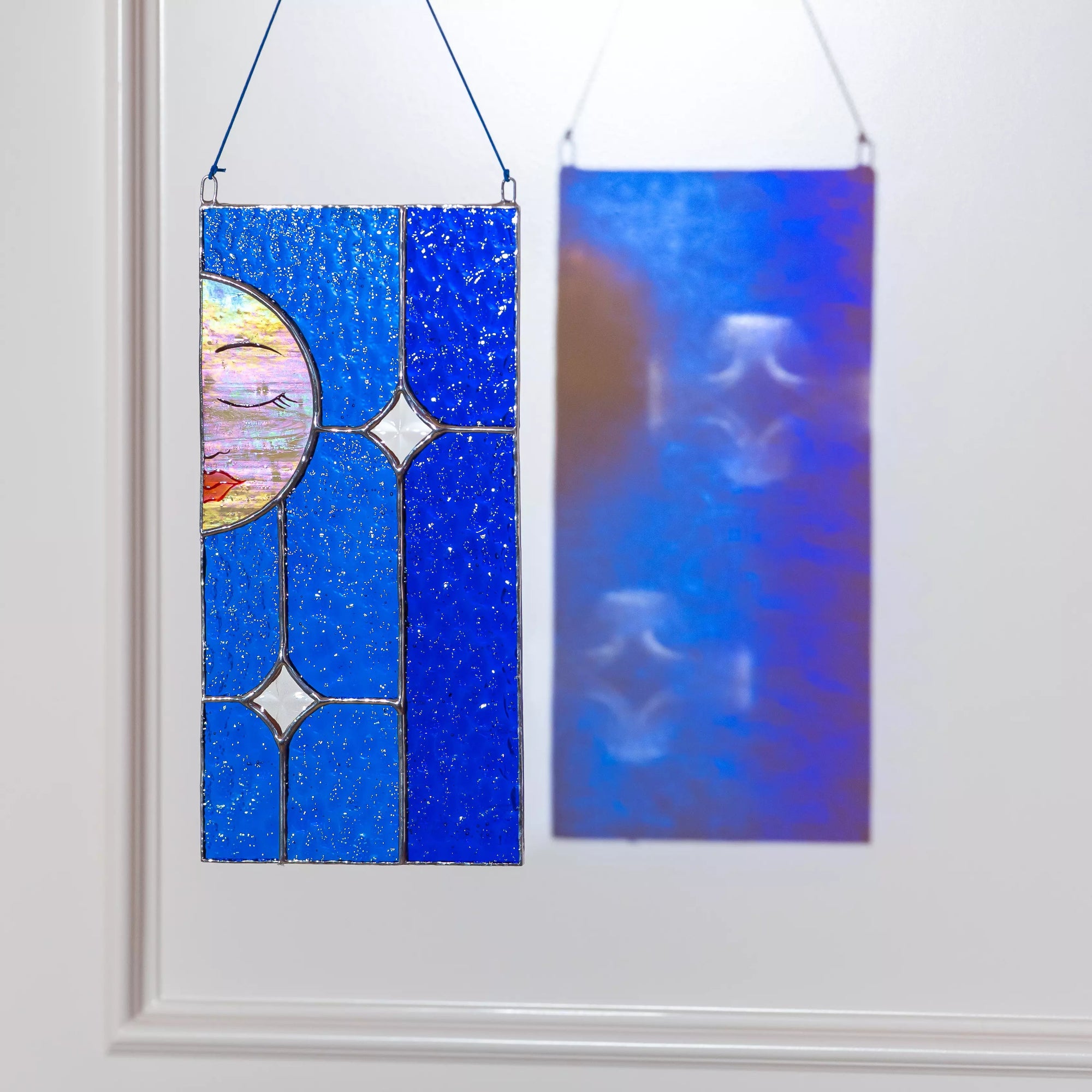 Stained glass panel with moon and multicolored design hanging on a white wall.