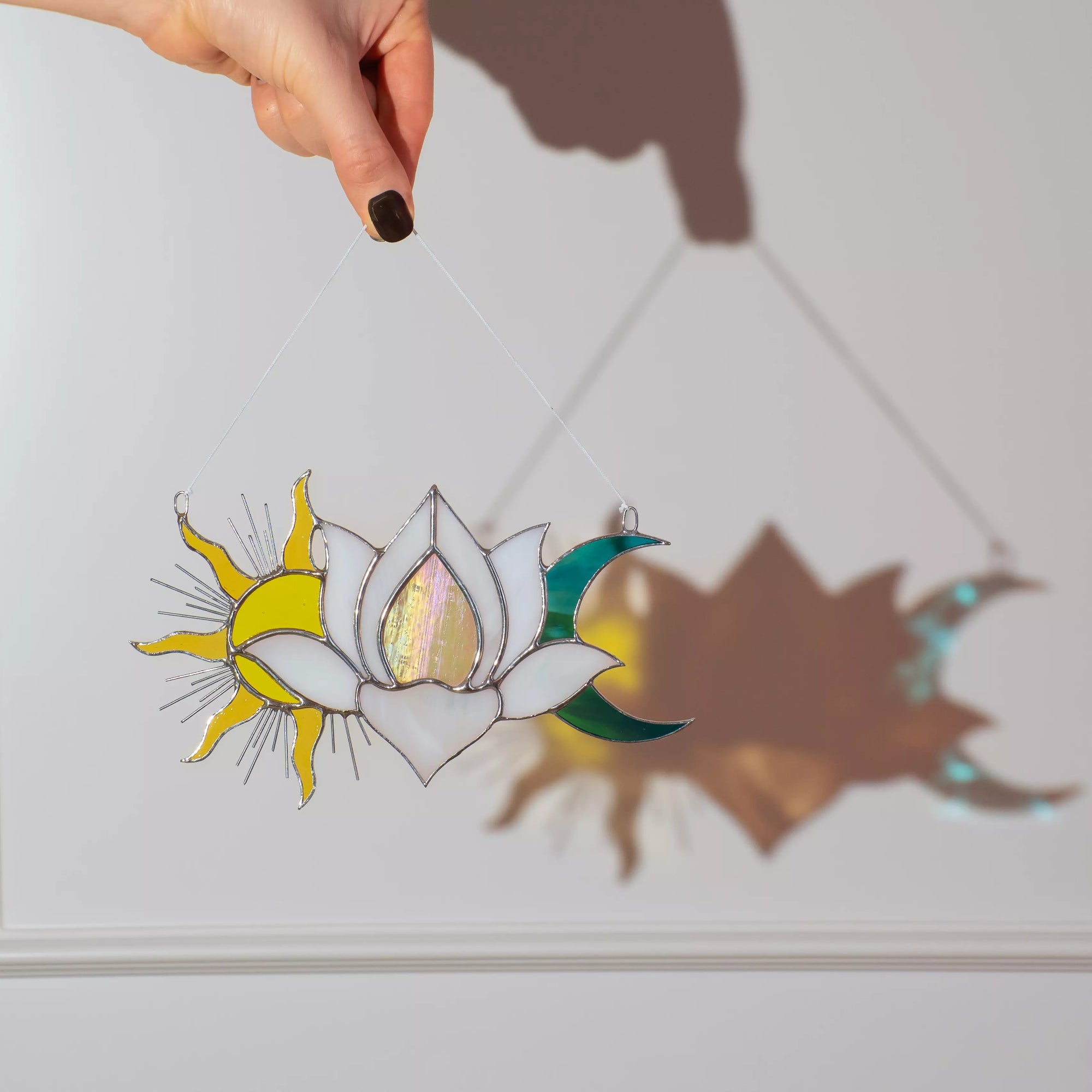 Decorative stained glass panel with sun, moon, and lotus design casting a shadow on a white surface.