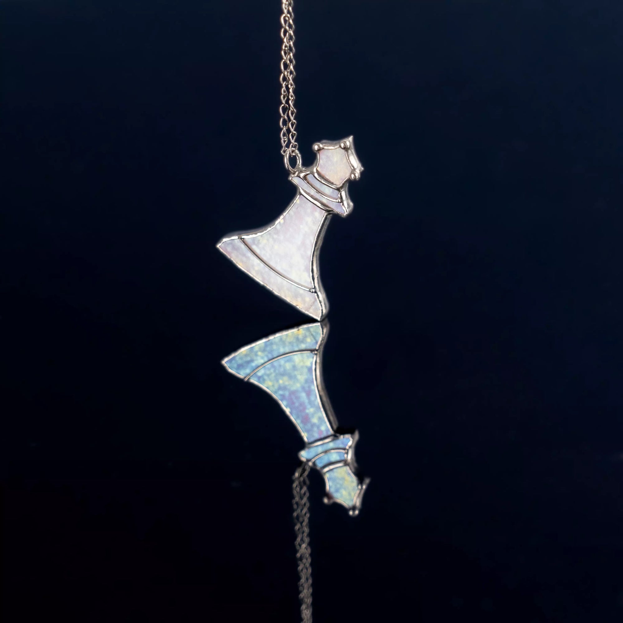 White opal queen stained glass pendant reflected on dark mirror surface, showing iridescent details and handmade precision.