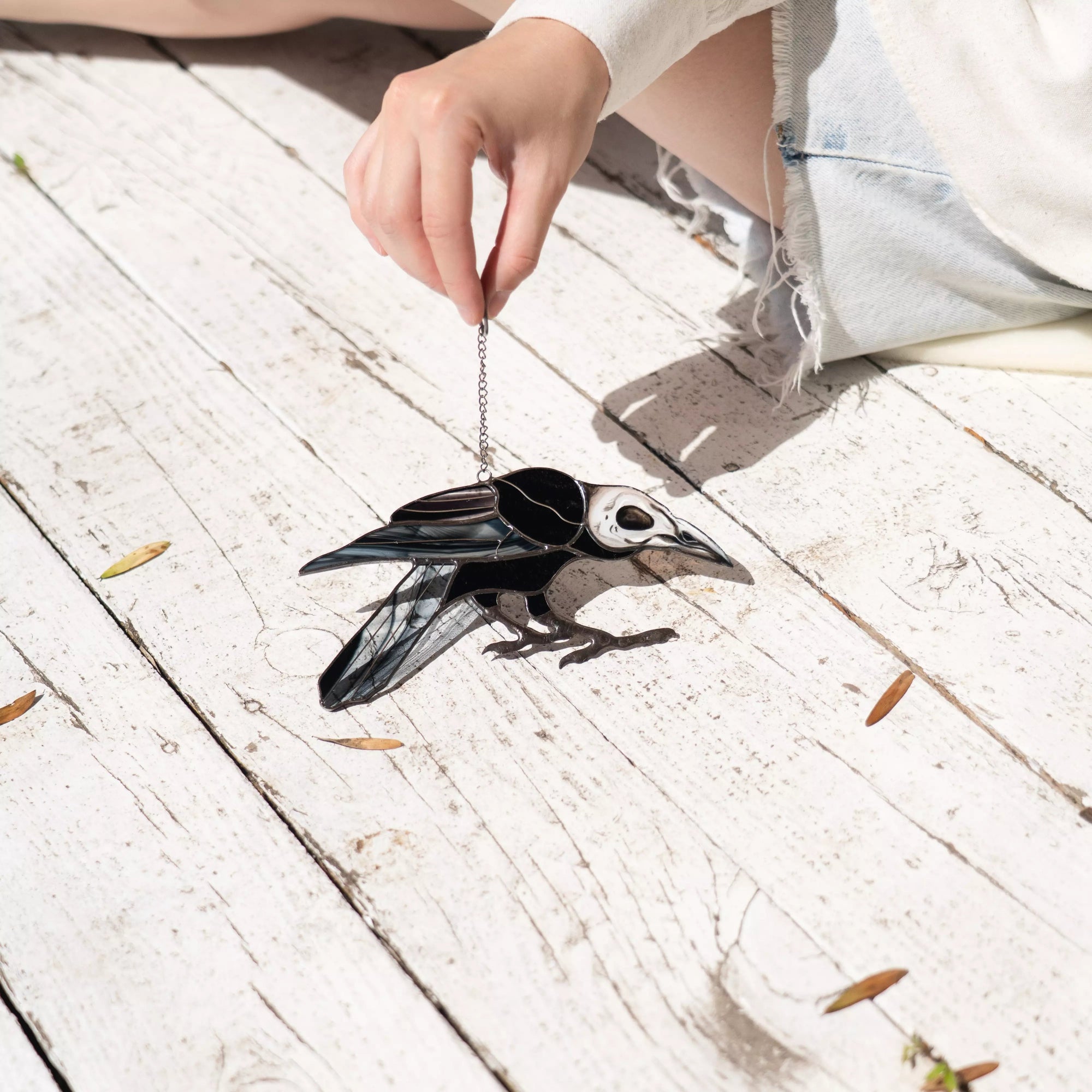 Black raven stained glass suncatcher on a white wooden floor with a person's hand holding it.