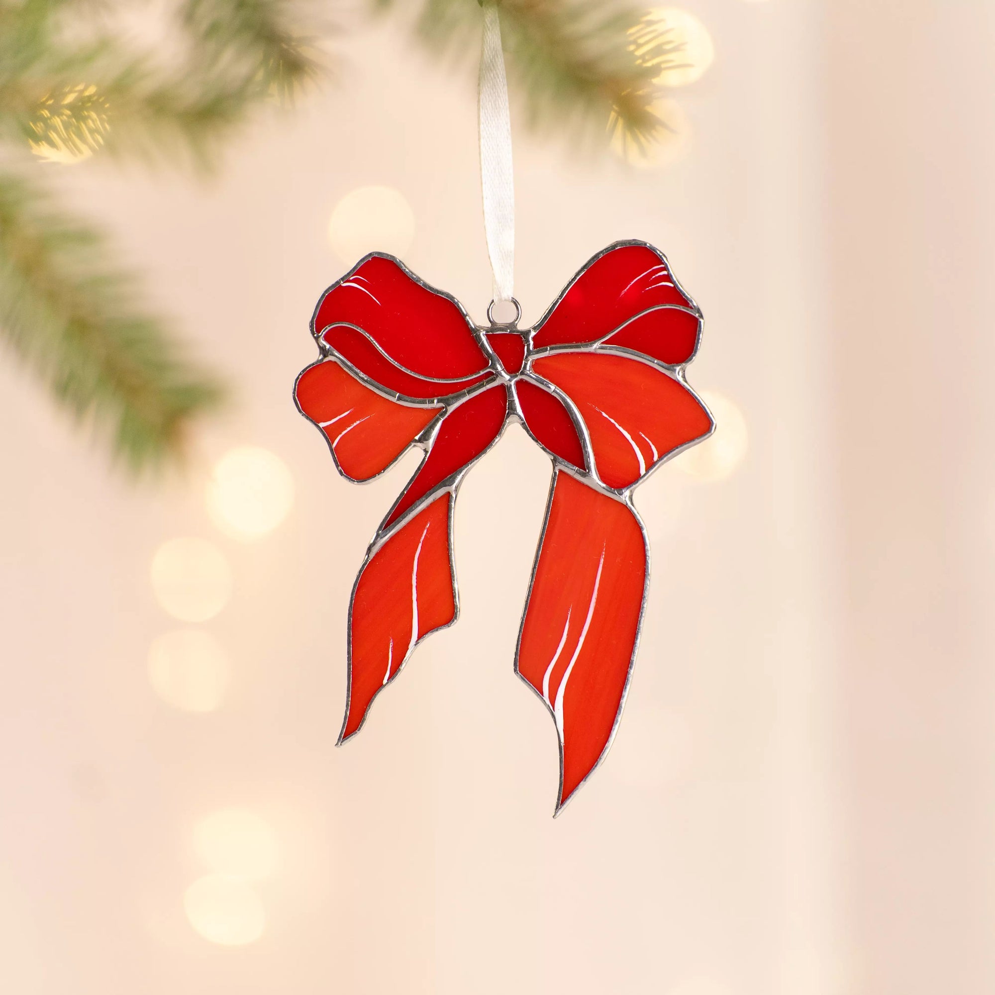 Stained glass suncatcher red bow ornament on a blurred Christmas tree background
