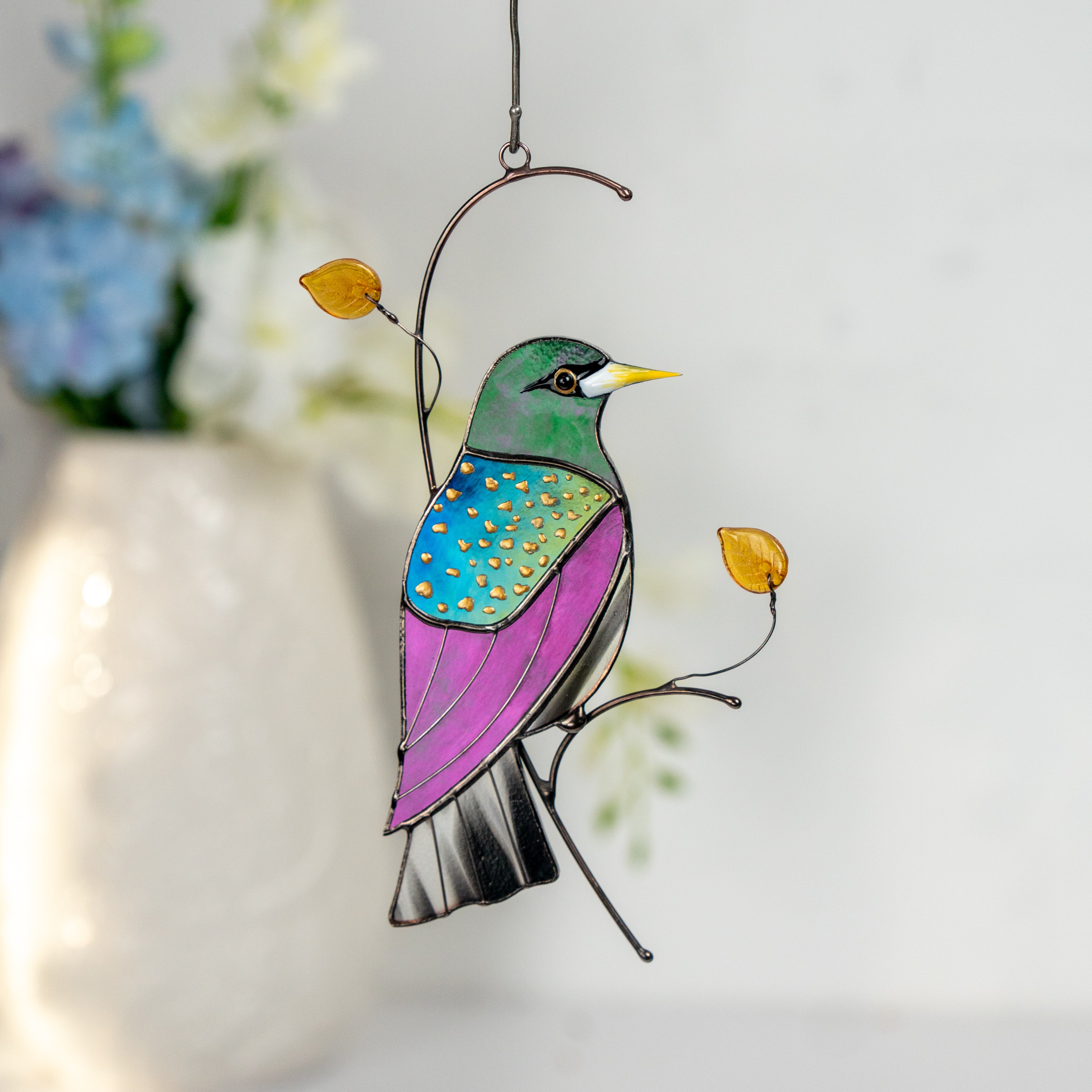 Stained glass starling bird suncatcher with glass leaves and beads, glowing in sunlight.