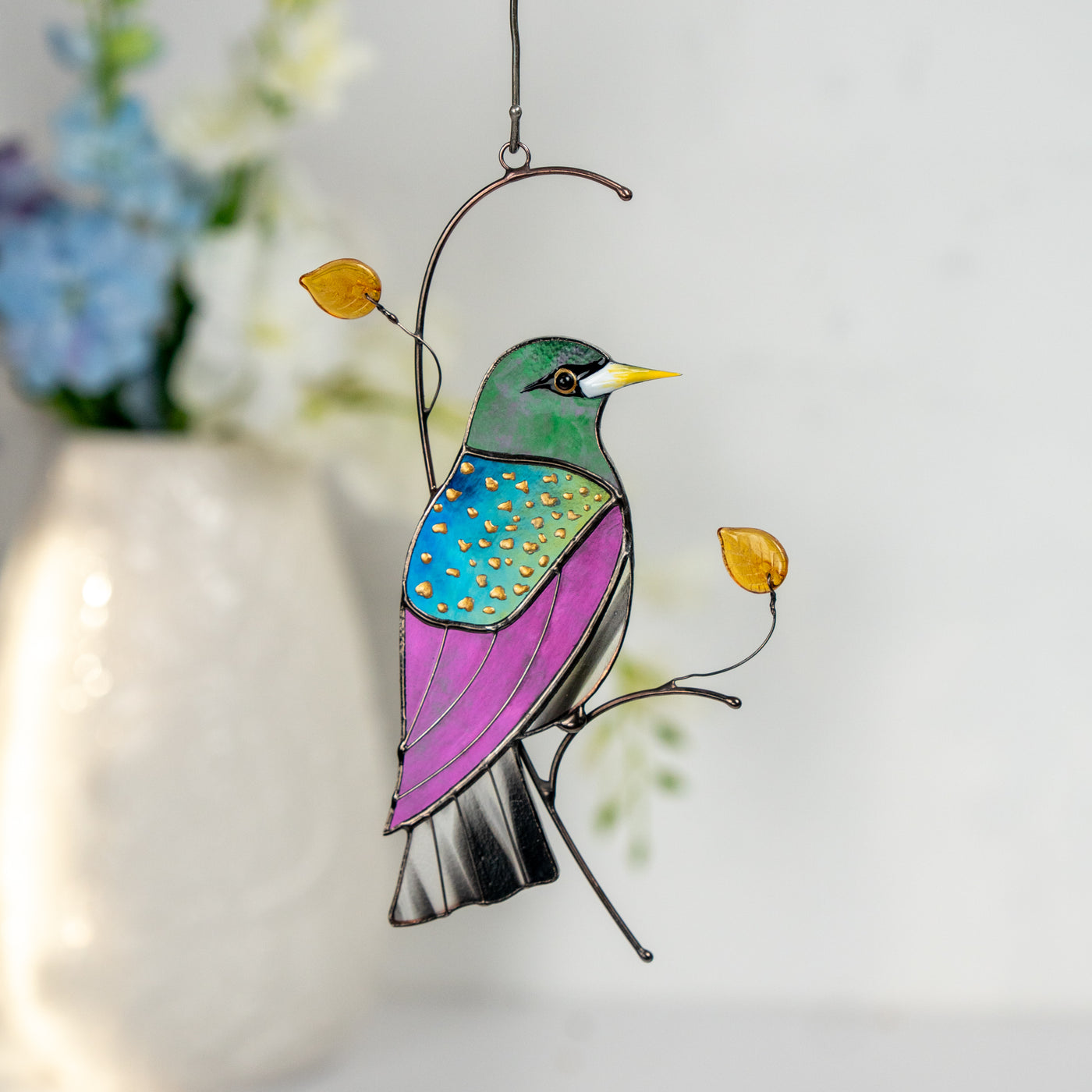 Stained glass starling bird suncatcher with glass leaves and beads, glowing in sunlight.