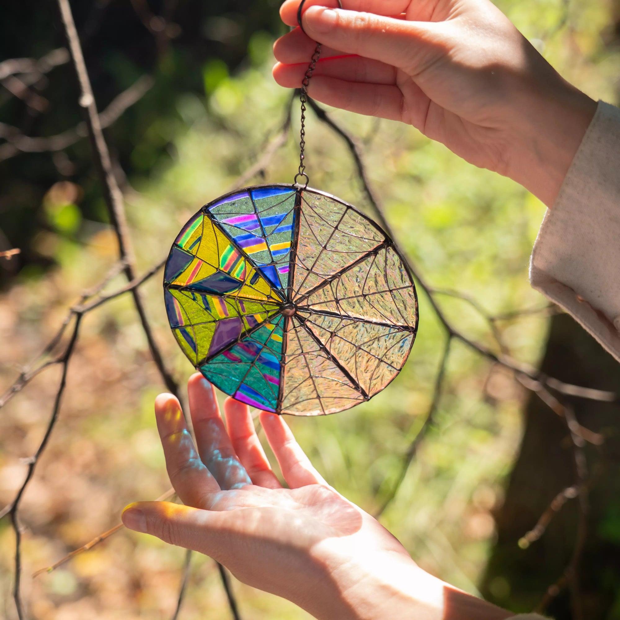 Hand holding a colorful stained glass suncatcher with it casting a soft shadow, against a natural background