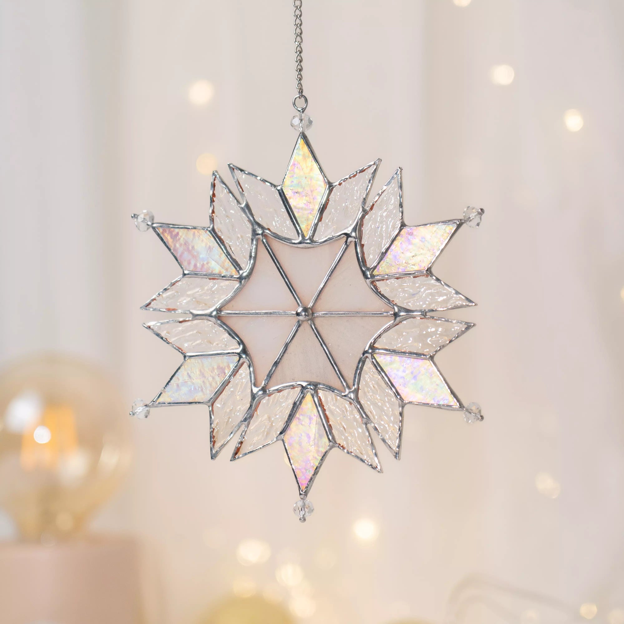 Stained glass snowflake Christmas ornament on a blurred background with lights.