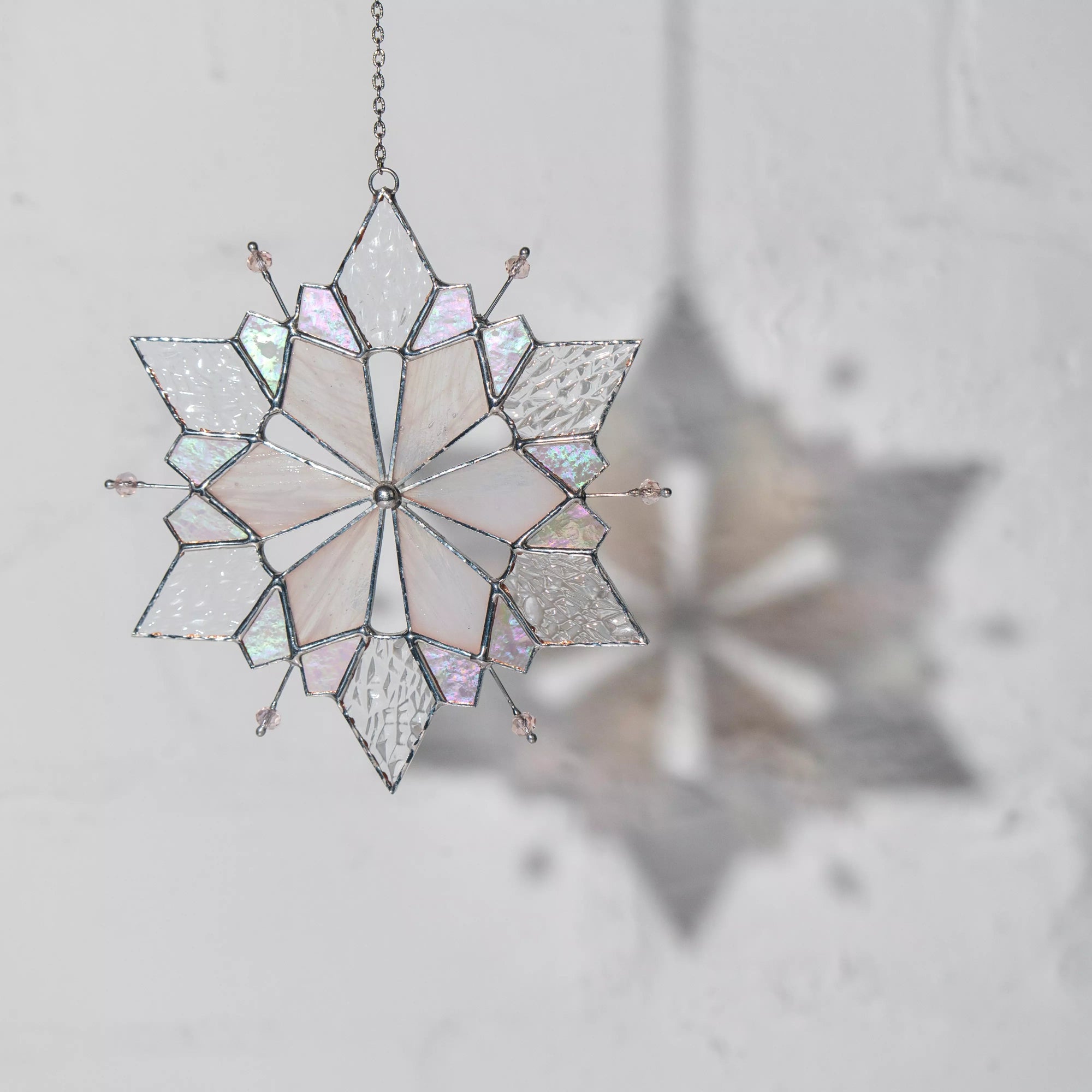 Stained glass snowflake hanging ornament on a light gray background, casting a soft shadow 