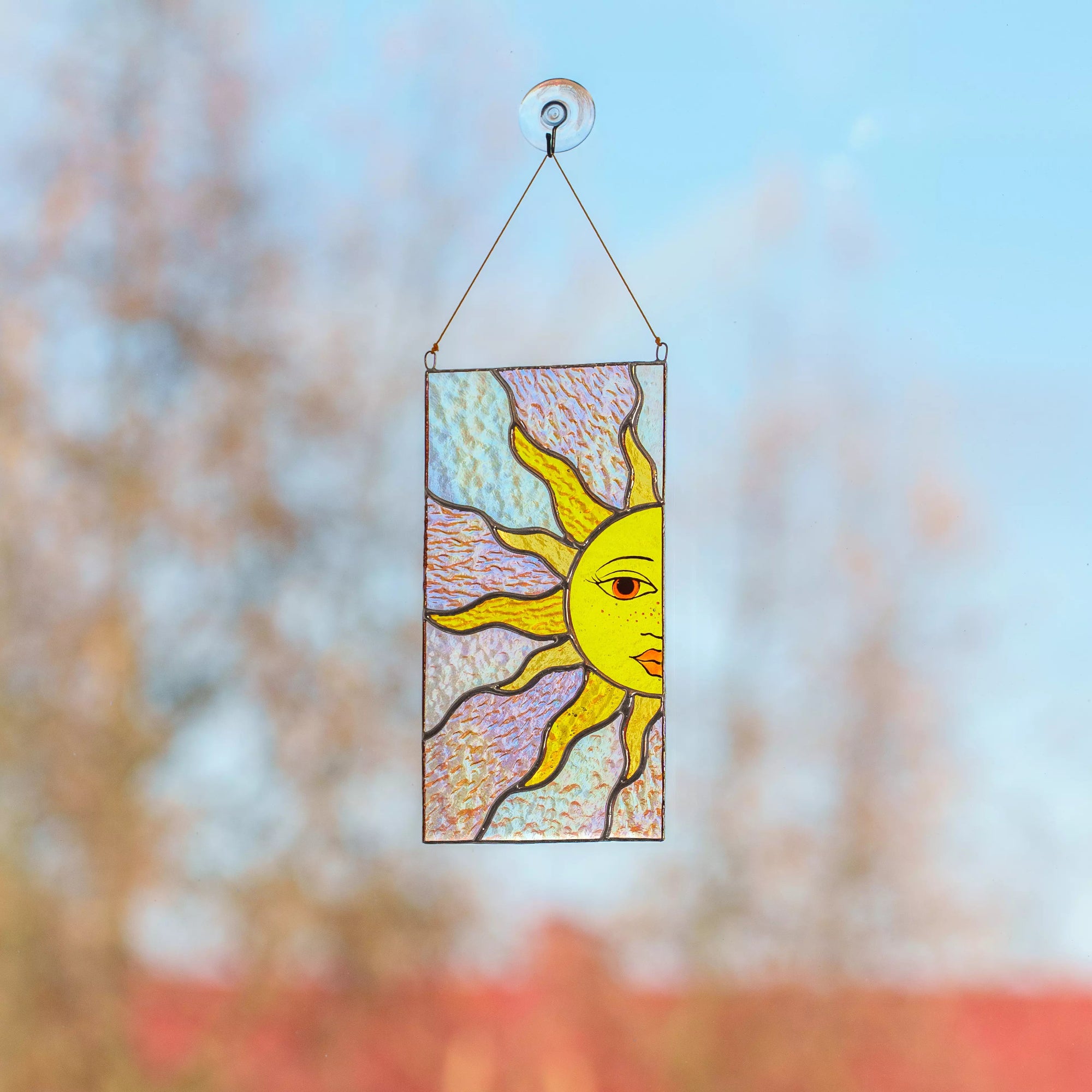 Stained glass sun panel hanging on a window with a blurred natural background