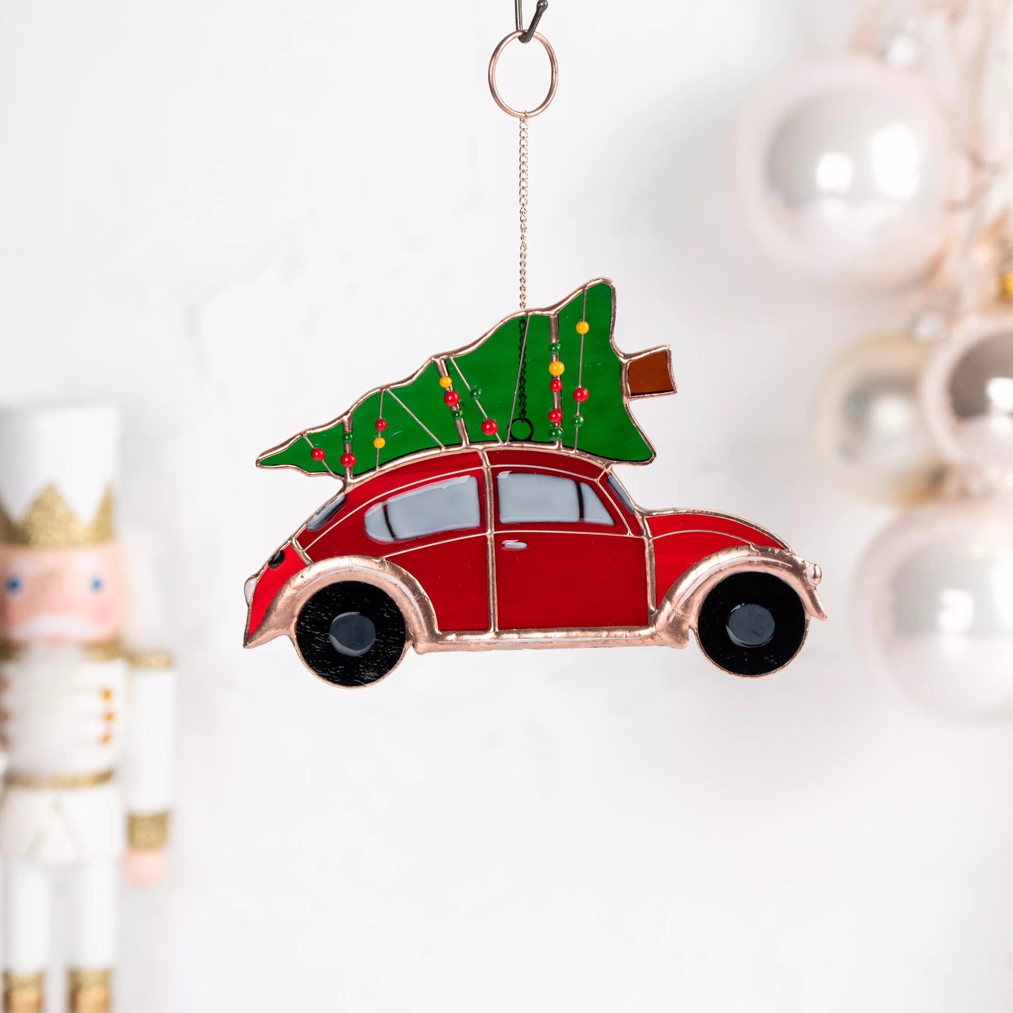Stained glass suncatcher featuring a red car with a Christmas tree on top, hanging against a blurred background.