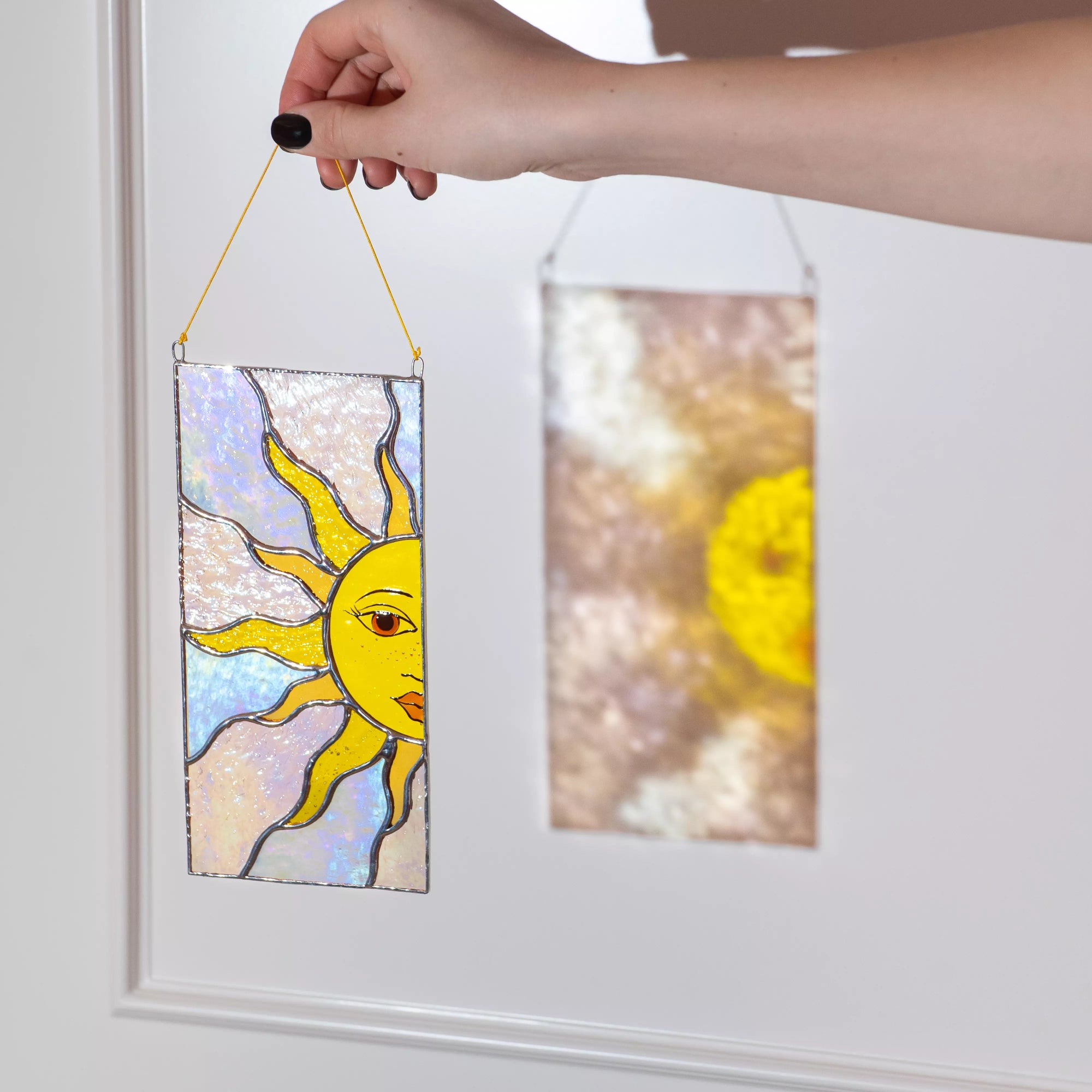 A hand holding a rectangular stained glass suncatcher that casts a beautiful reflection on the wall.