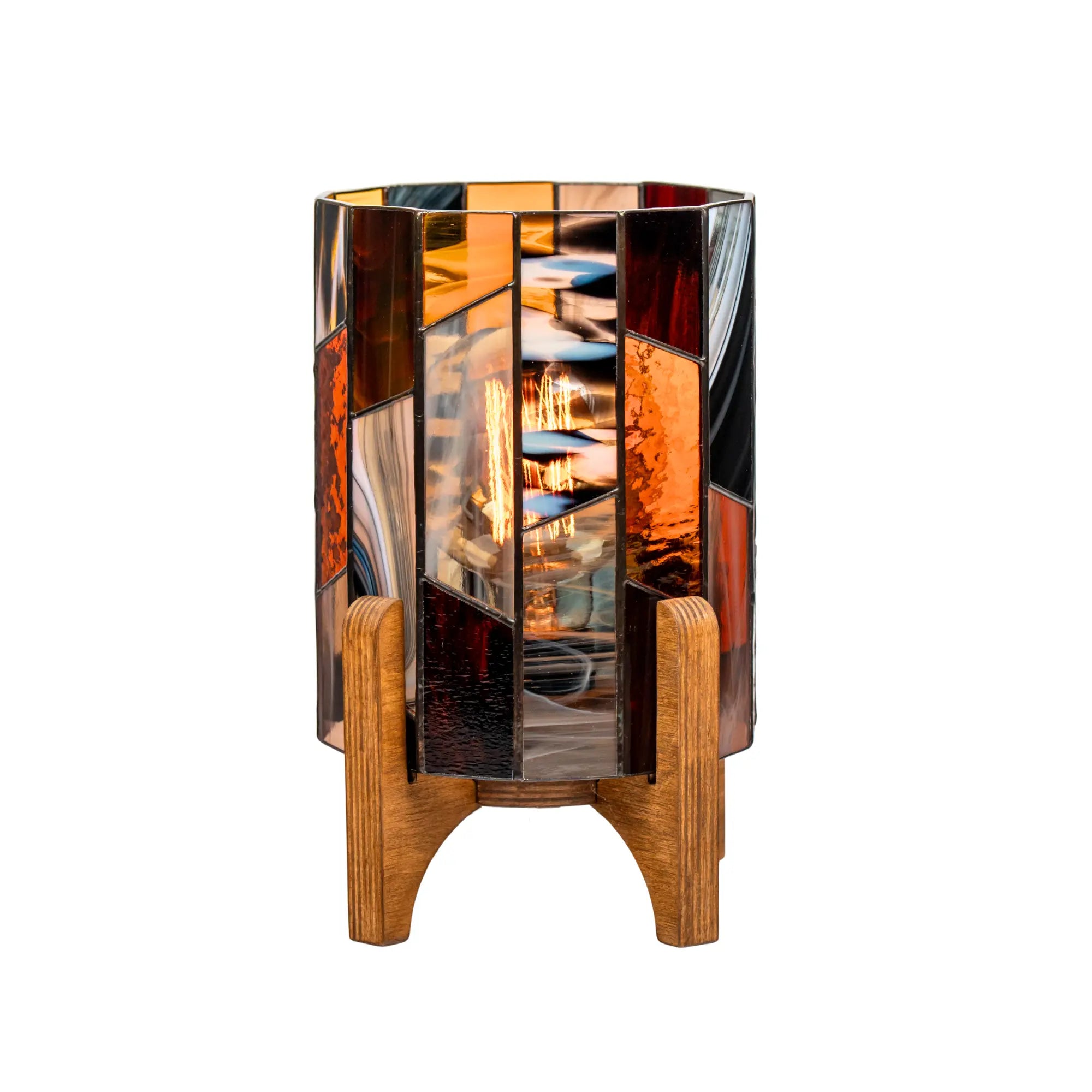Stained glass table lamp with geometric amber, brown, and gray glass panels on a wooden base, handmade home decor emitting warm cozy light.