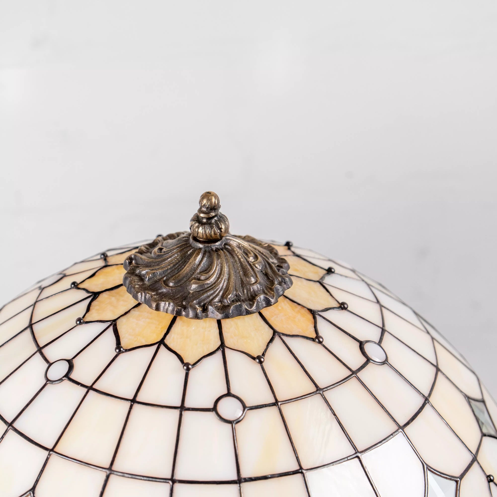 Close-up of bronze finial on stained glass dome with creamy white and amber petal shapes
