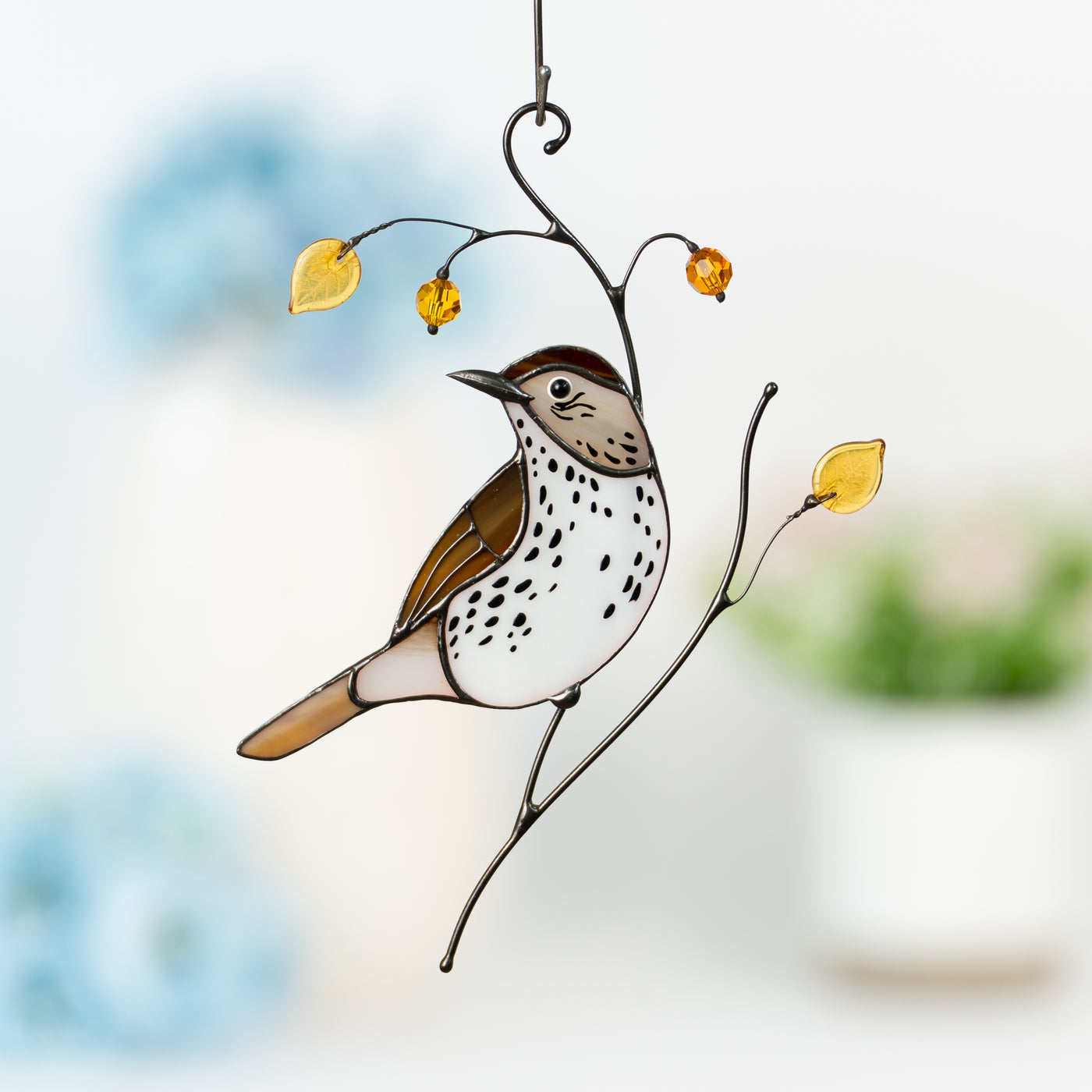 Elegant stained glass wood thrush with spotted belly, yellow leaves, and warm-toned beads against a soft floral background