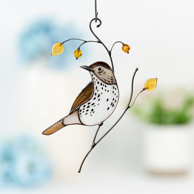 Elegant stained glass wood thrush with spotted belly, yellow leaves, and warm-toned beads against a soft floral background