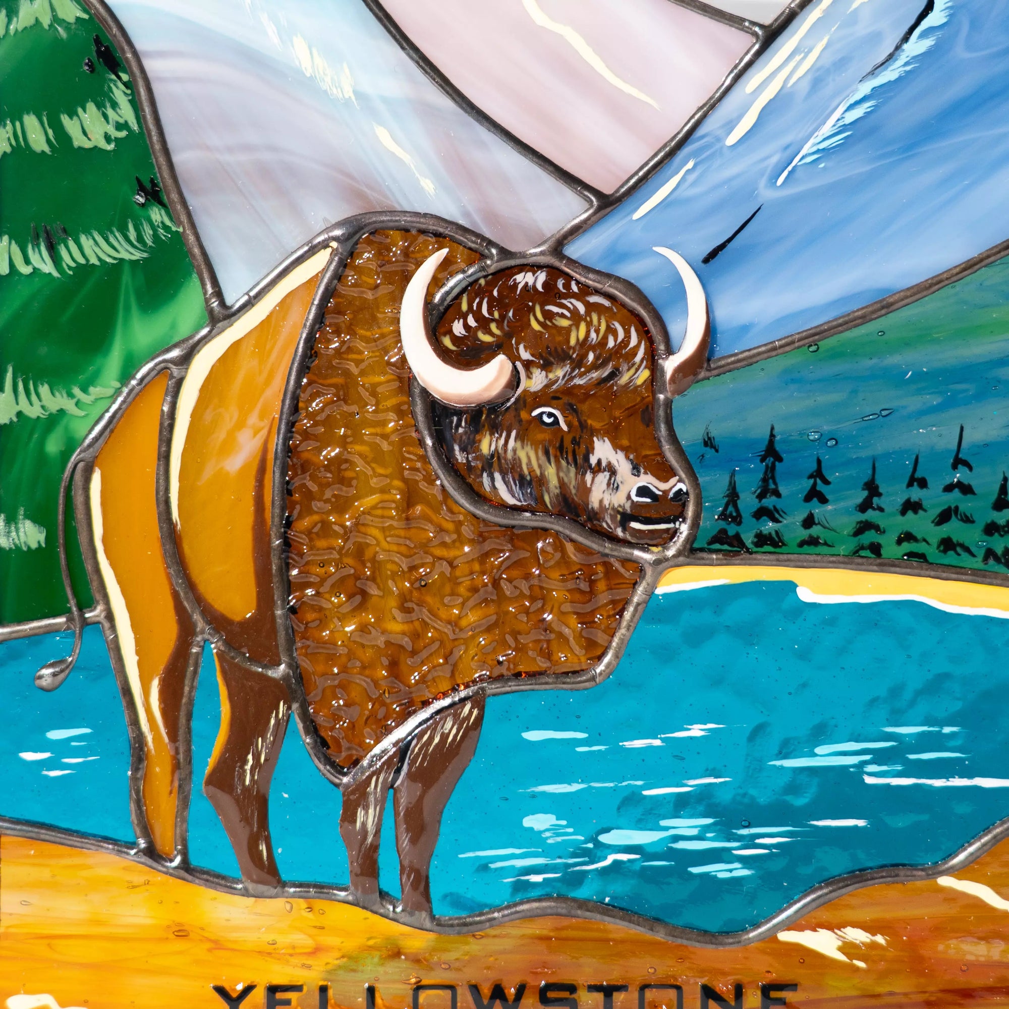 A close-up view of the bison and mountain details in a handcrafted stained glass suncatcher casting a shadow.
