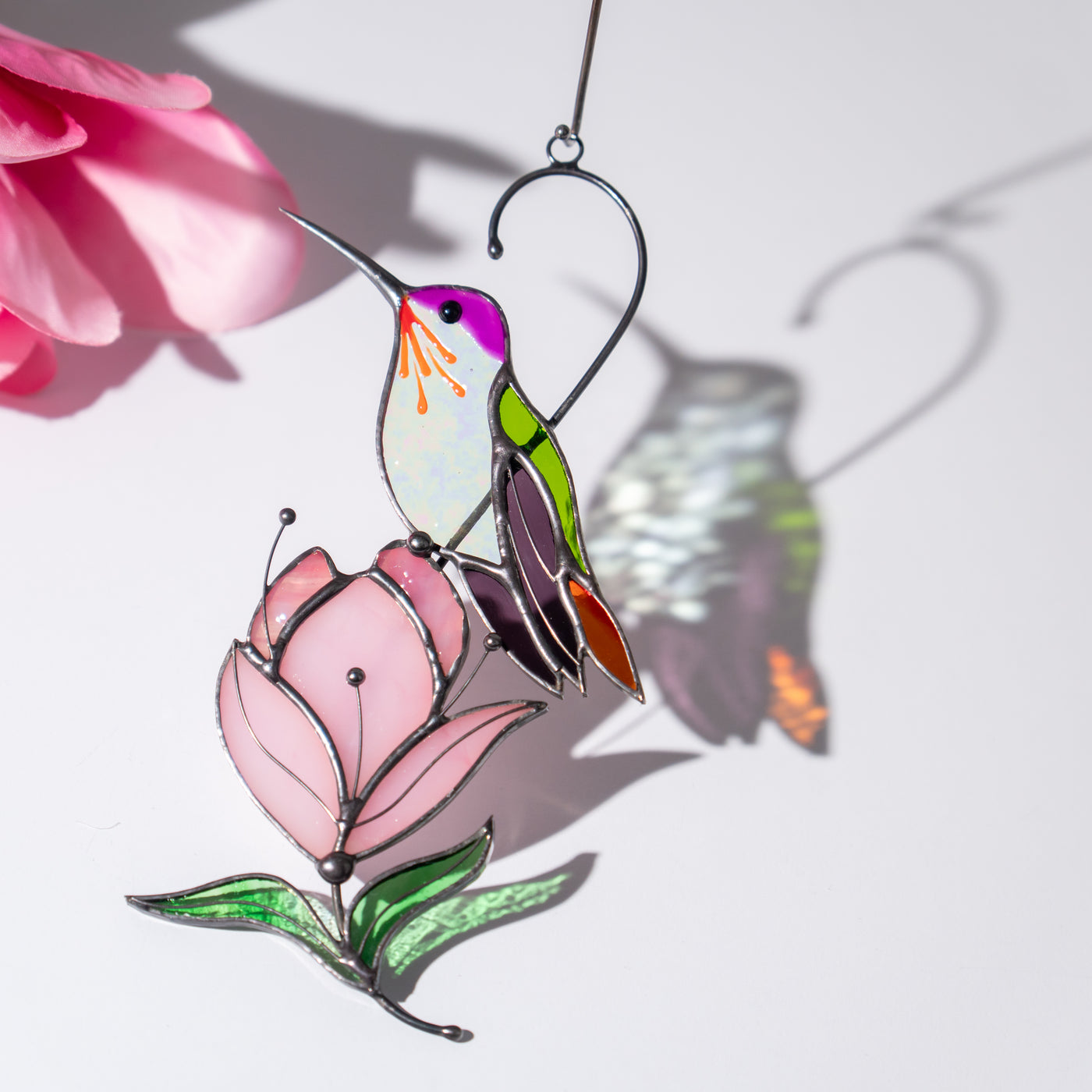 Colorful hummingbird suncatcher with pink flower and сolorful shadows on a white background.