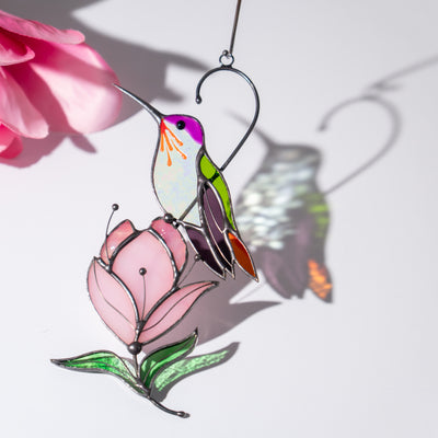Colorful hummingbird suncatcher with pink flower and сolorful shadows on a white background.