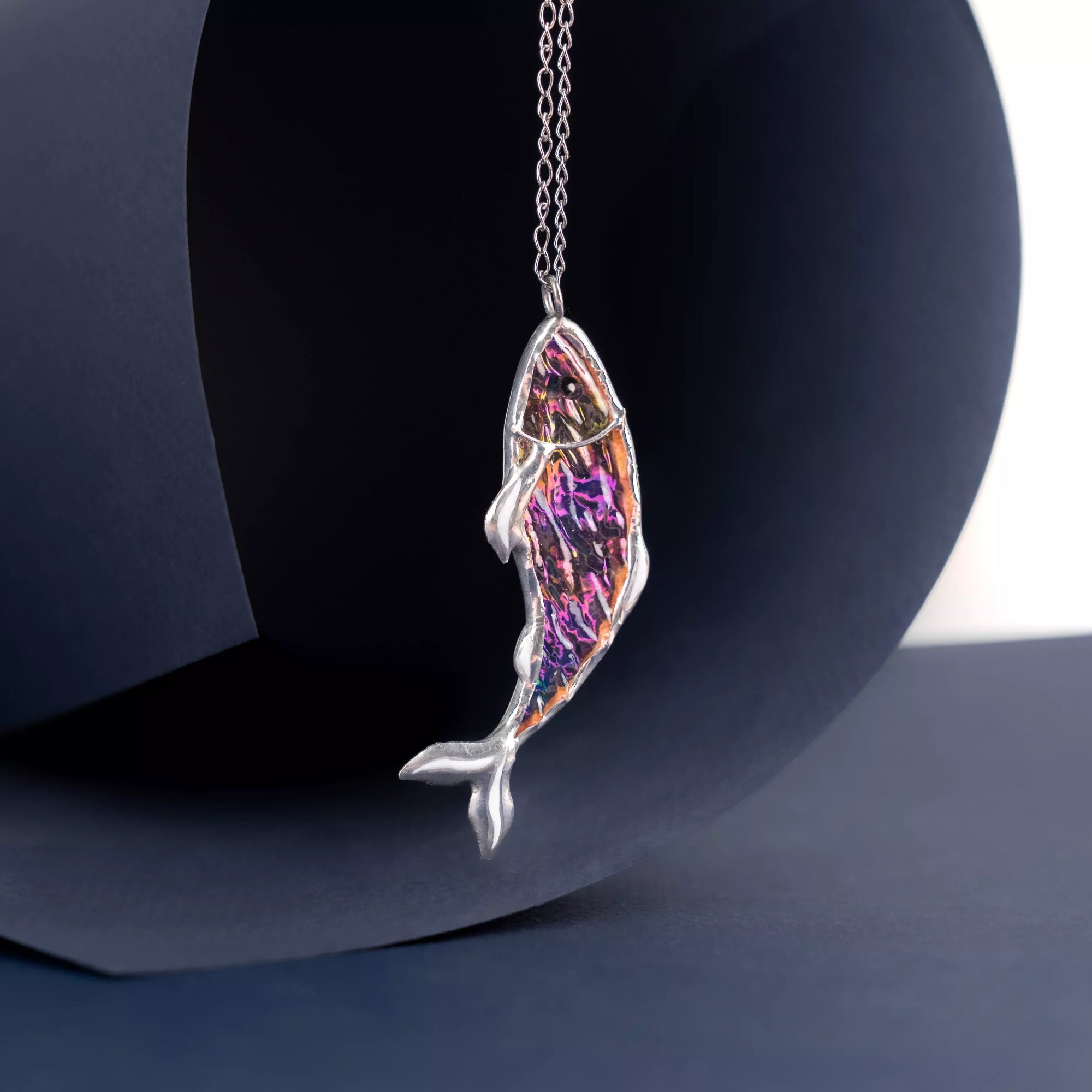Irisated fish-shaped pendant on a chain against a dark background
