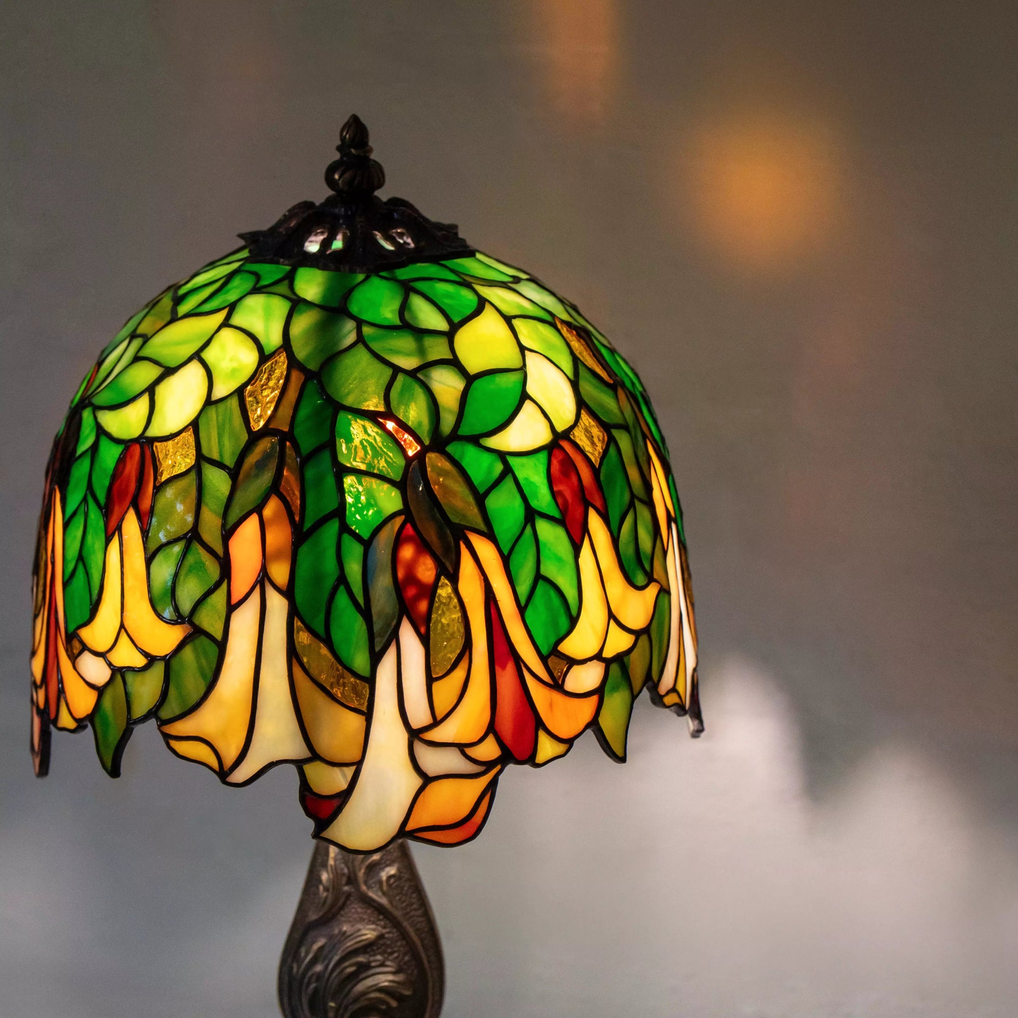 Close-up of Tiffany style lamp shade with green, yellow and amber glass petals forming a cascading floral pattern.