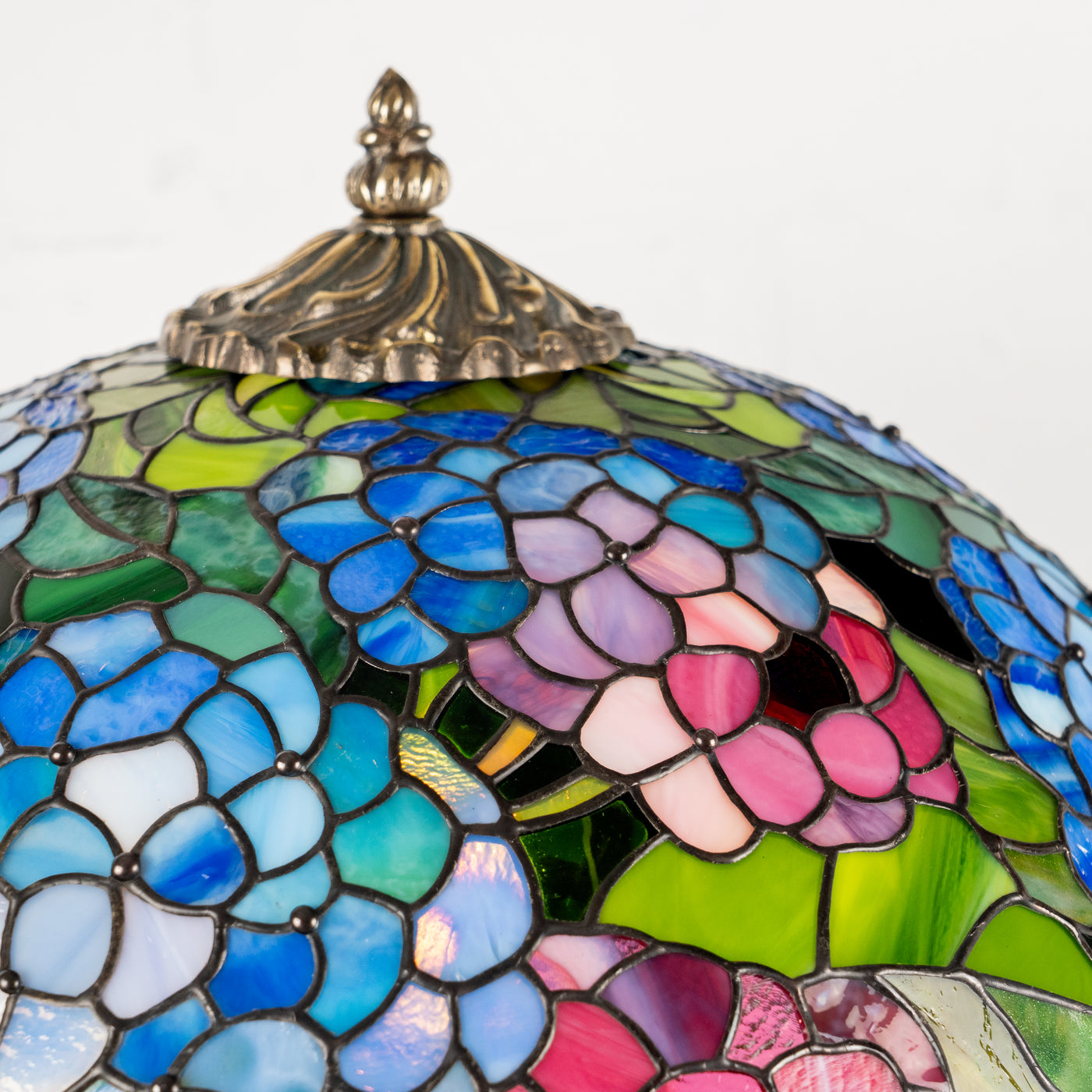Ornate lamp top with stained glass blue hydrangeas and floral pattern in close-up.
