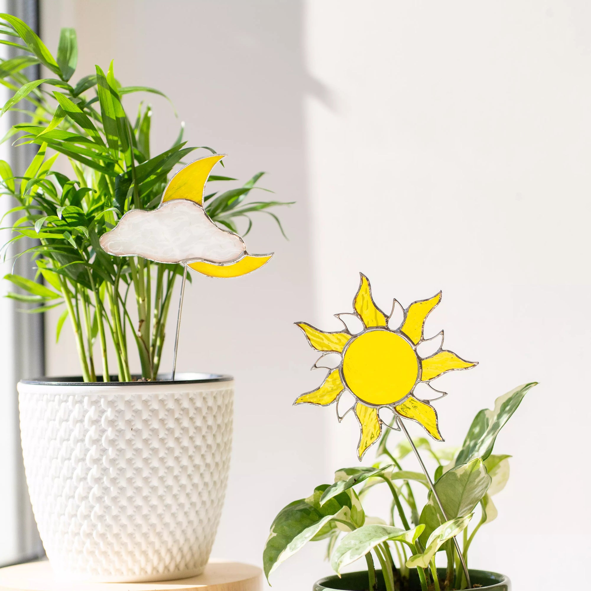 Two stained glass sun and moon shapes in front of potted plants.