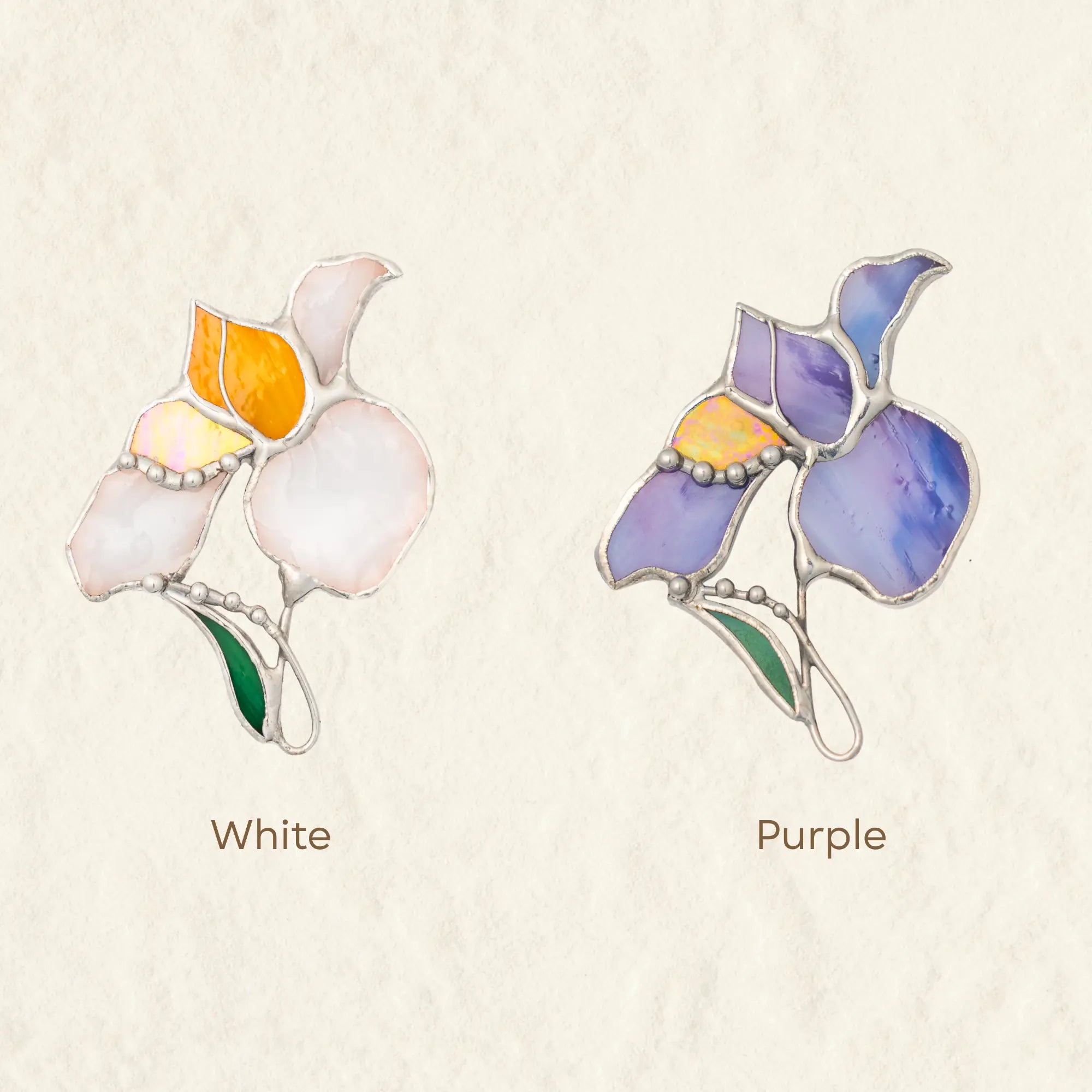 Variation of two stained glass iris brooches, one white and one purple, on a beige background.