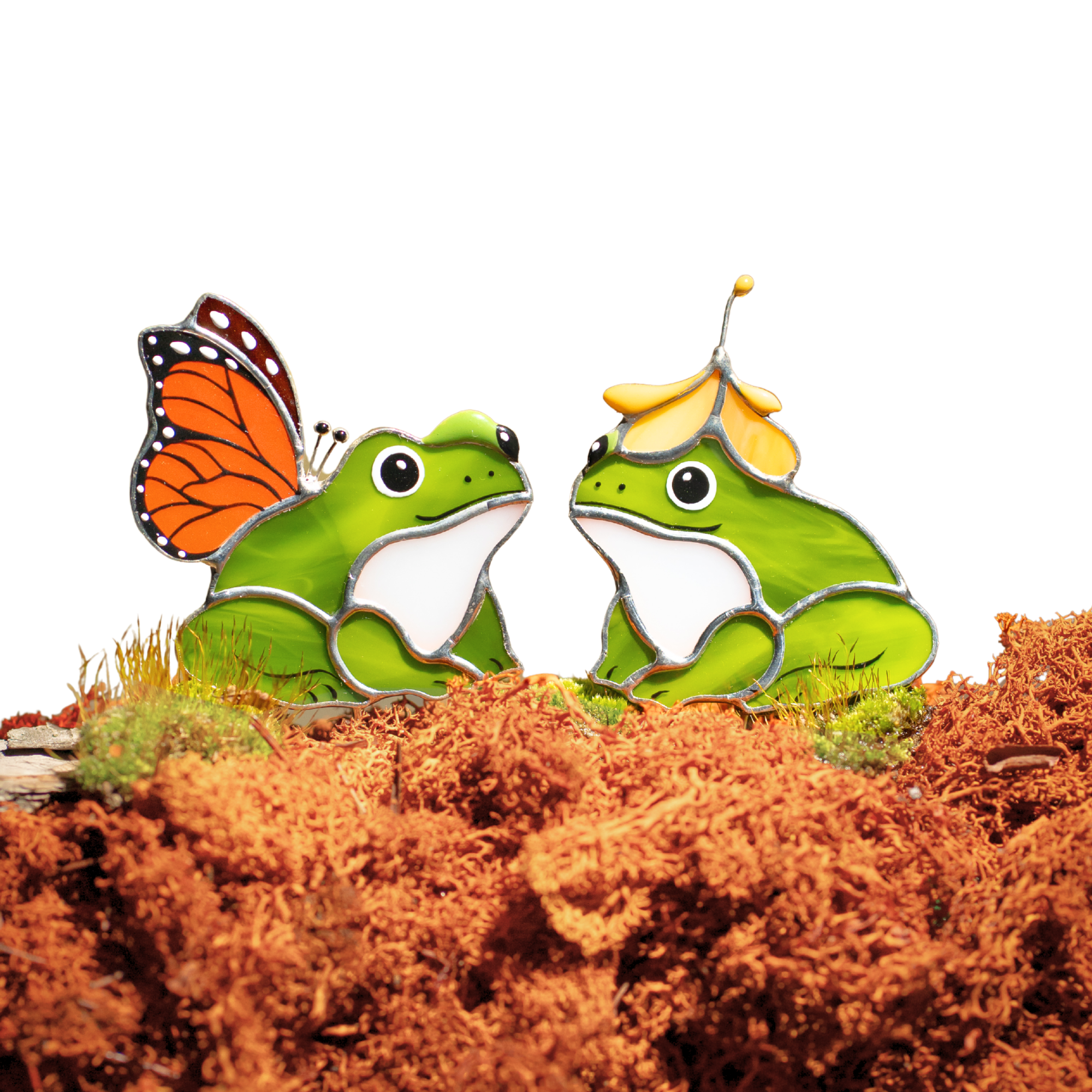 Two stained glass green frogs with butterfly and bee accessories on a brown surface.
