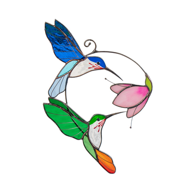Stained glass suncatcher with two hummingbirds and a pink flower, displayed in front of a vase.