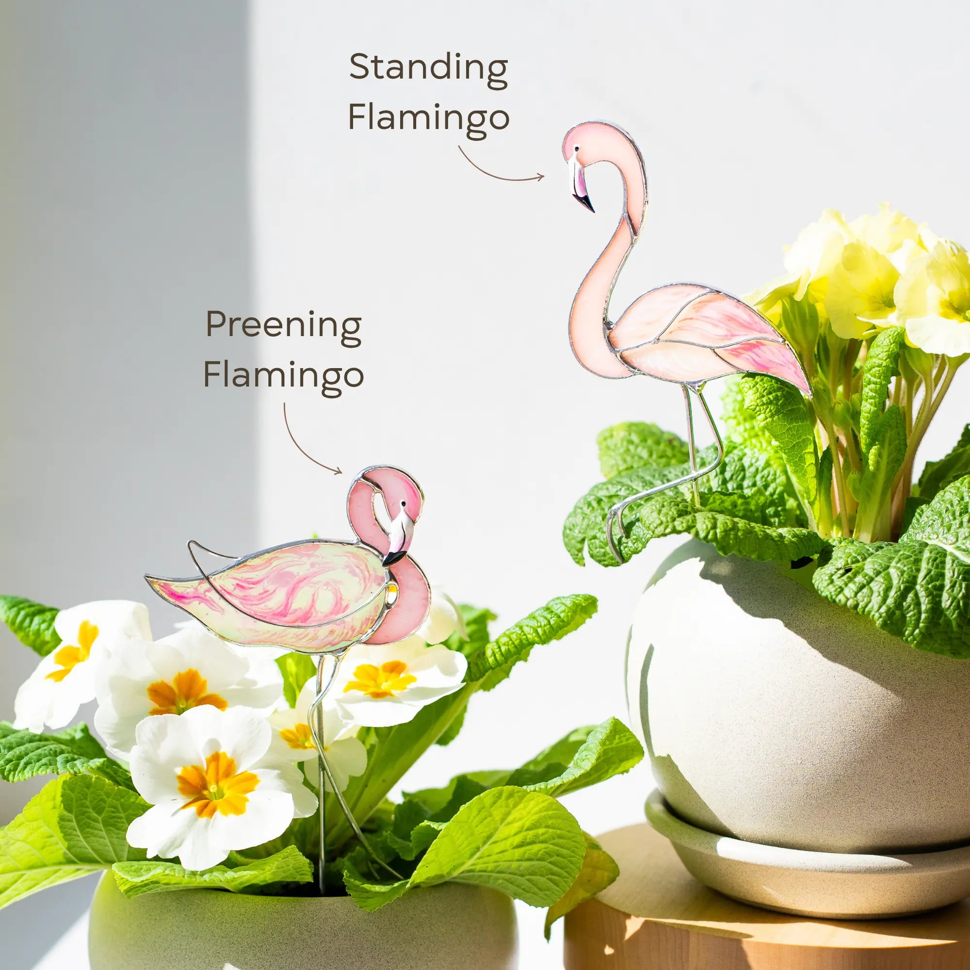 Variation of two stained glass flamingo plant stakes with flowers and leaves on a light background: preening and standing flamingos