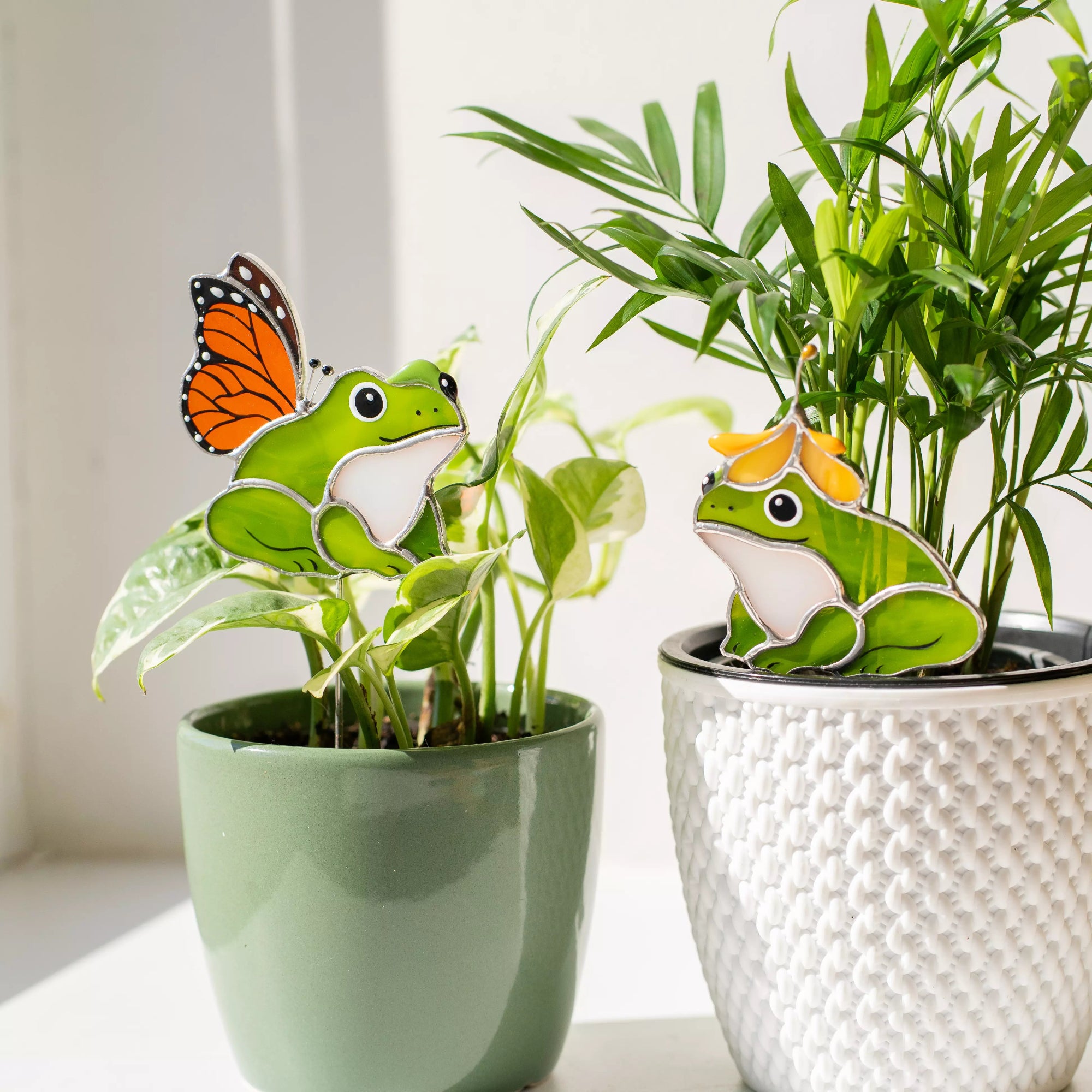 Two stained glass plant stakes with decorative frog and butterfly